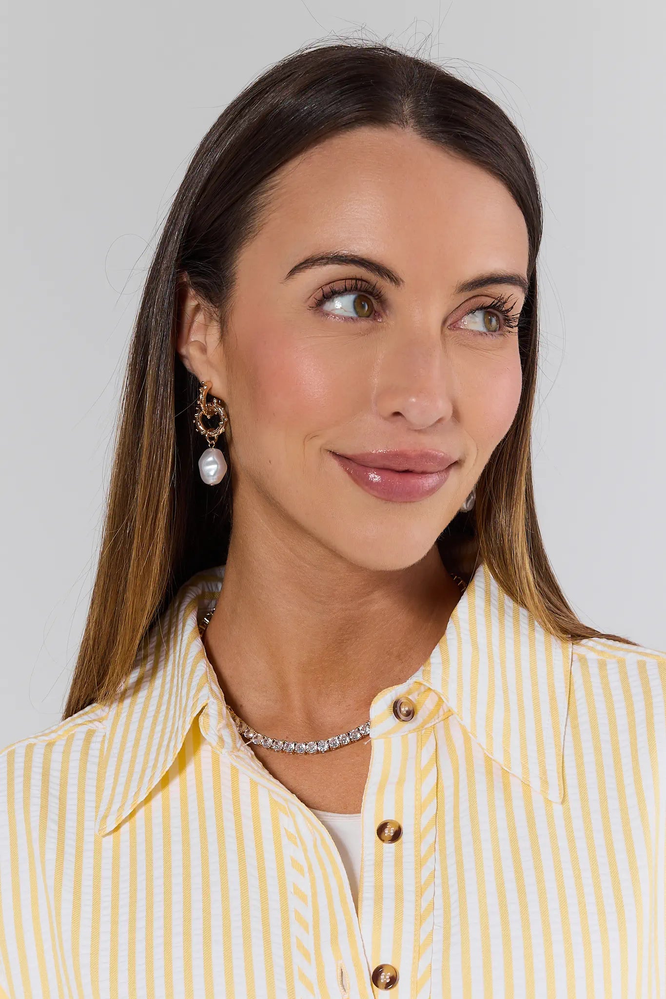 Woman wearing a yellow and white striped shirt with jewelry on a plain background