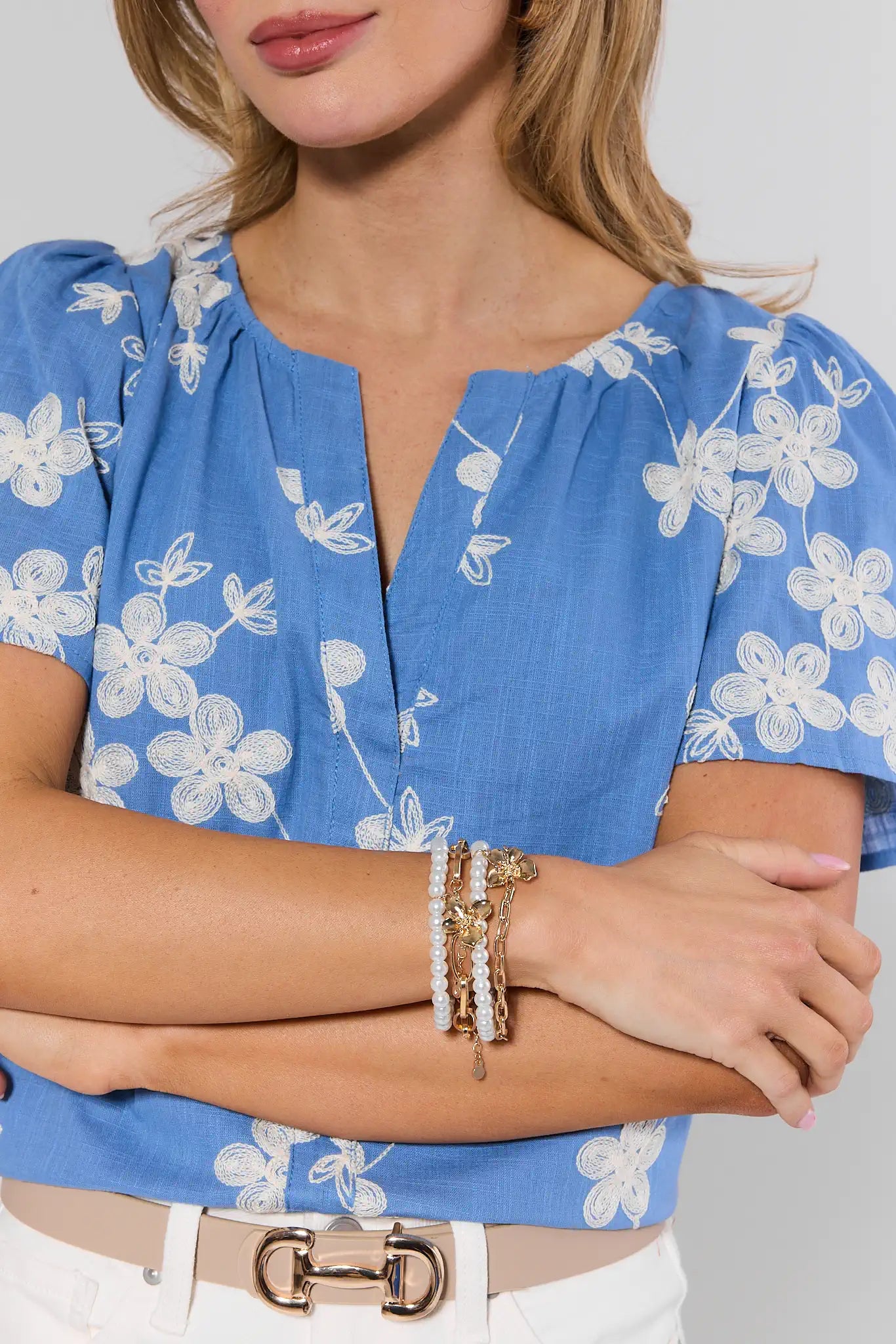Woman wearing a blue floral blouse with her arms crossed, wearing multiple bracelets.