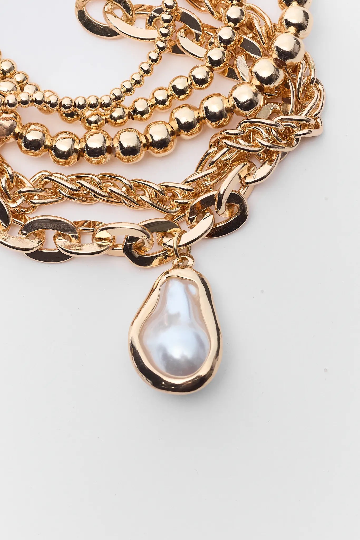 Stack of gold bracelets with a pearl charm on a light background
