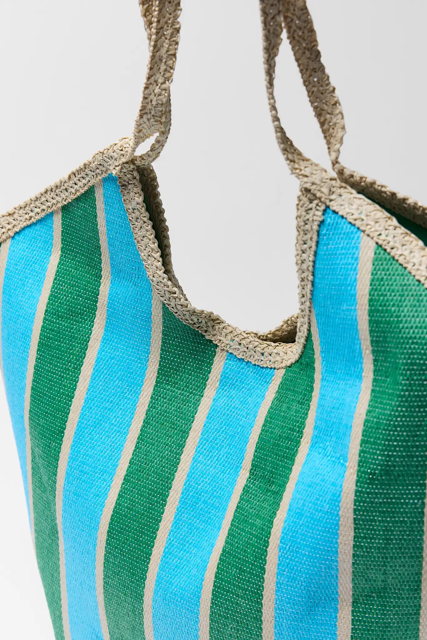 Striped green and blue bag with beige trim on a light gray background