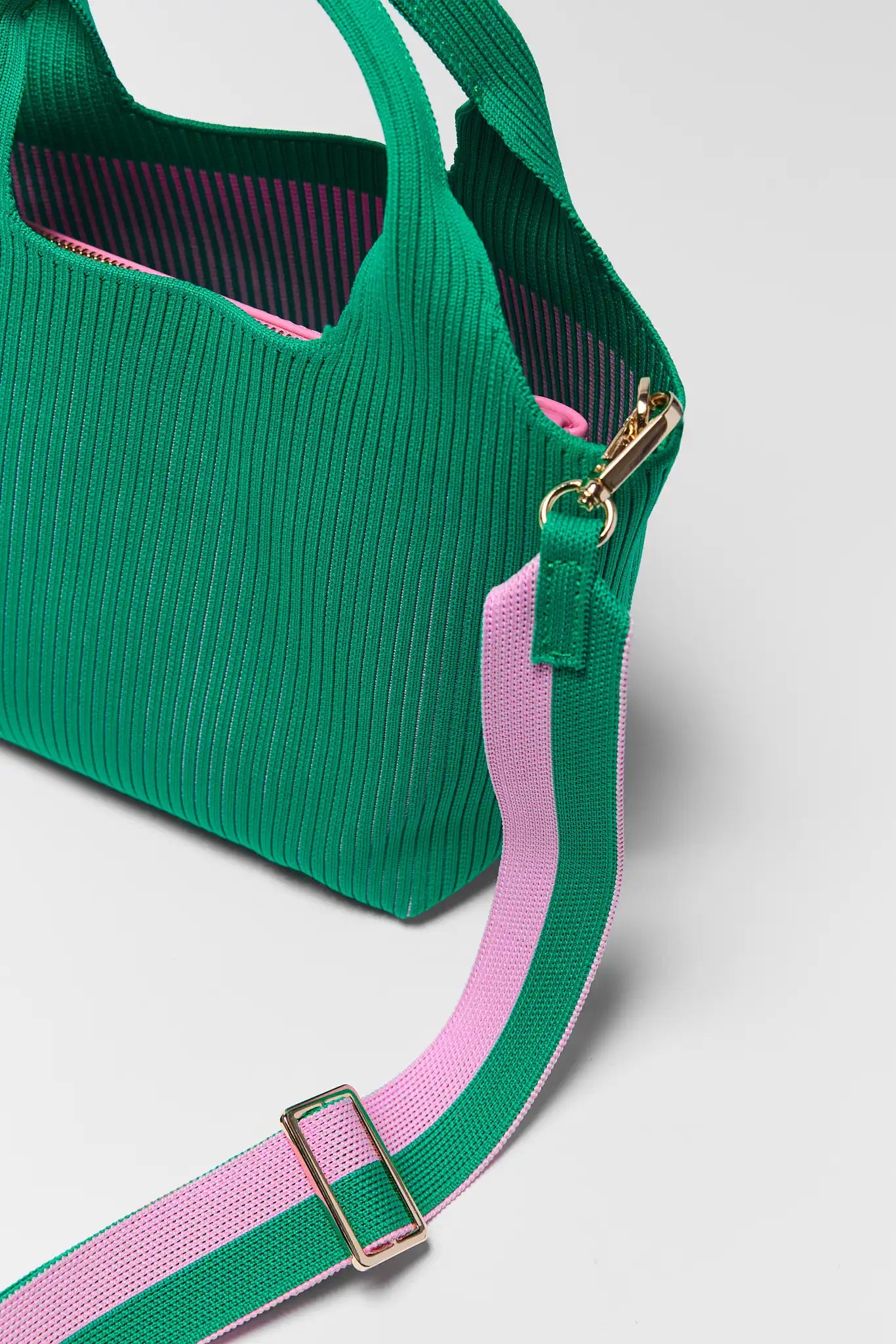 Green handbag with a pink strap on a light gray background