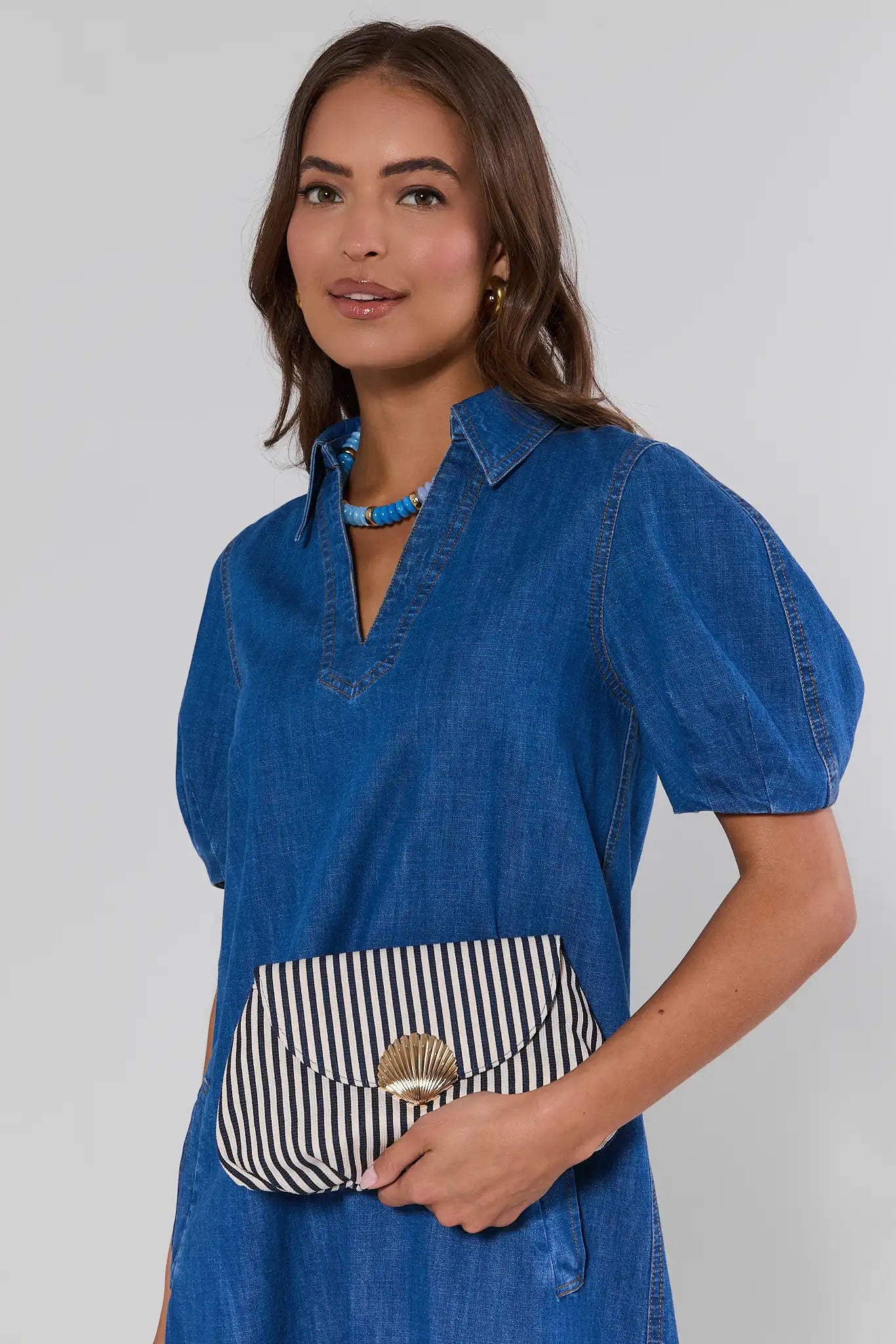 Woman wearing a blue dress holding a striped handbag against a plain background