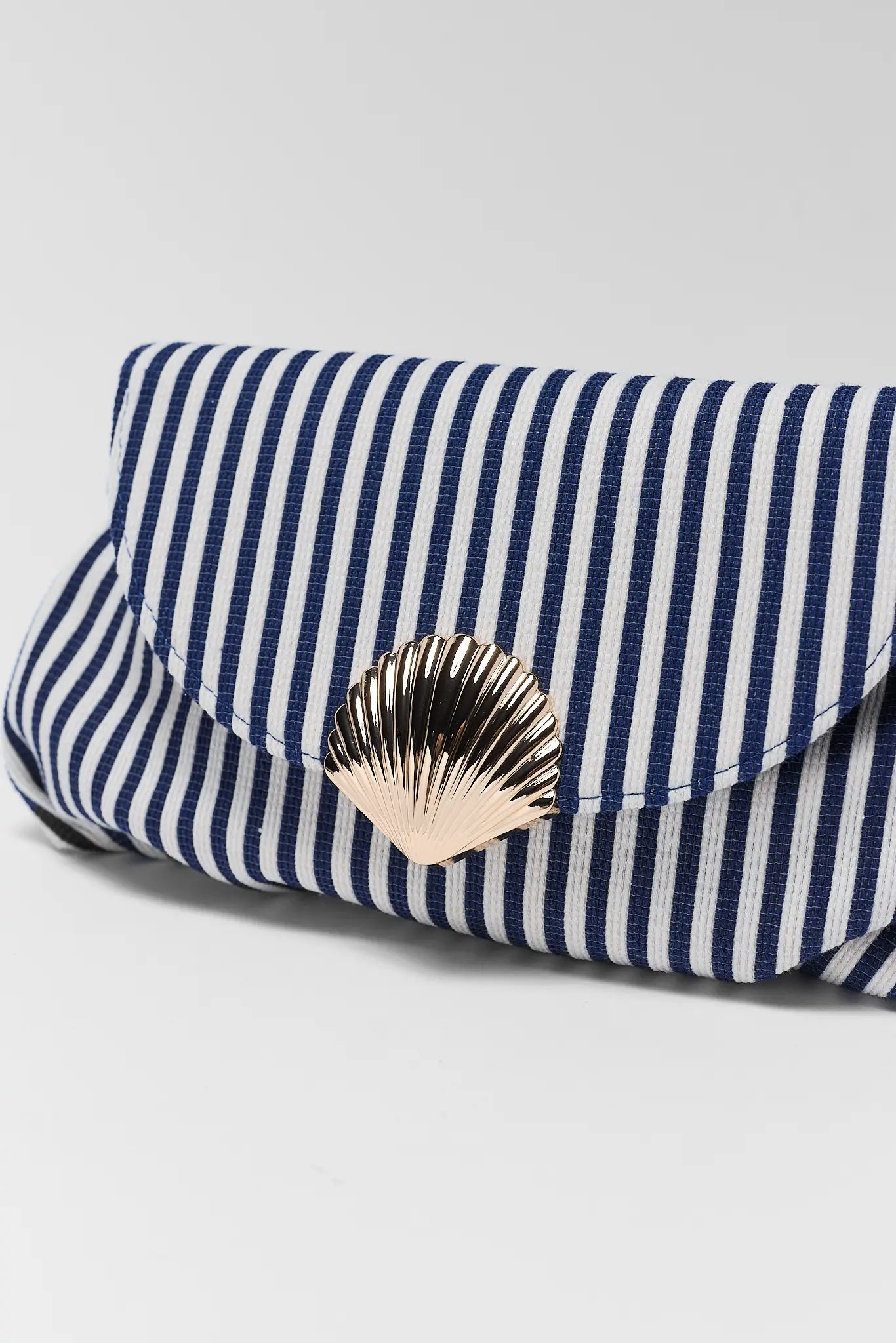 close up Navy and white striped clutch bag with a gold shell emblem on a light gray background