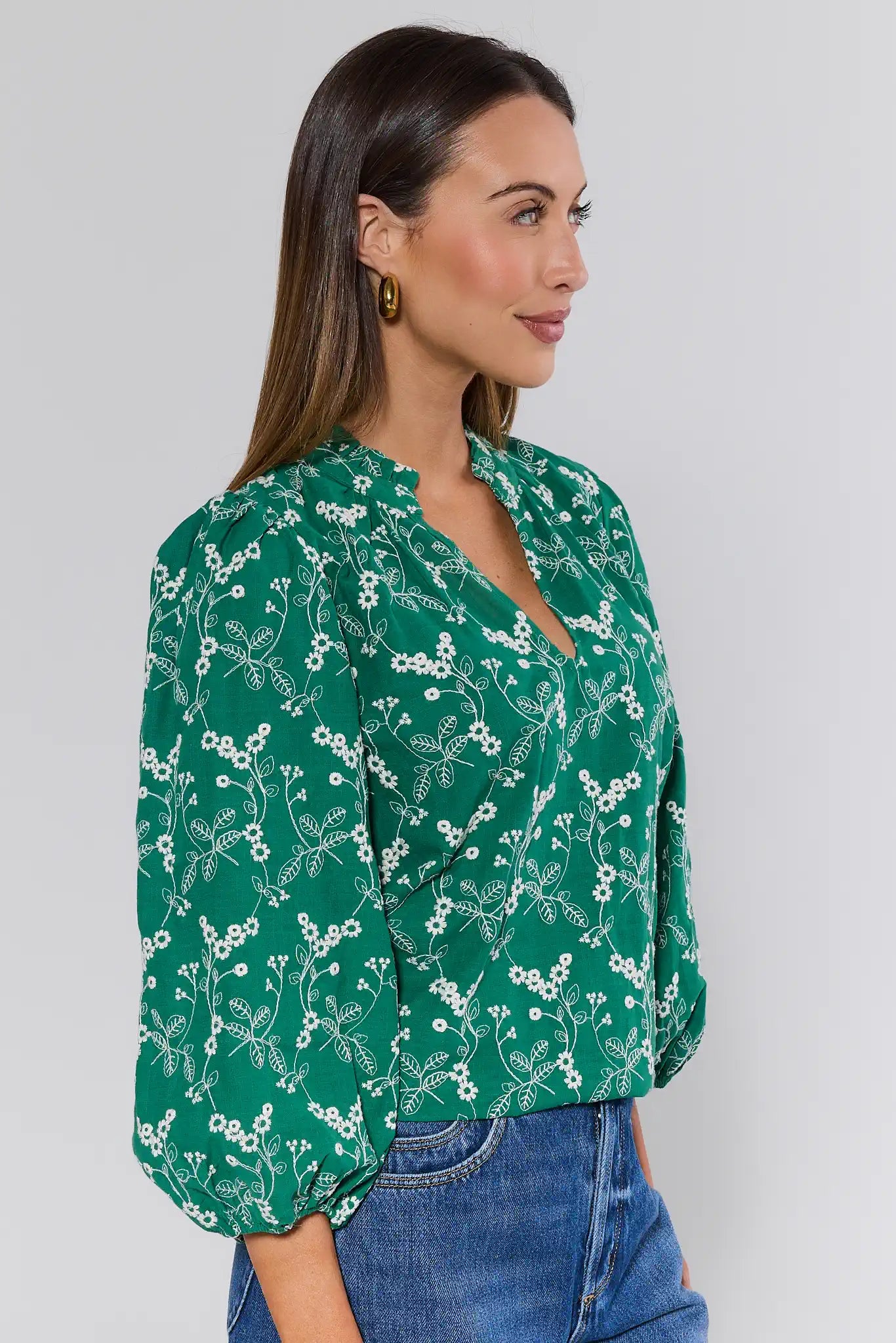 Woman wearing a green floral blouse and blue jeans against a white background