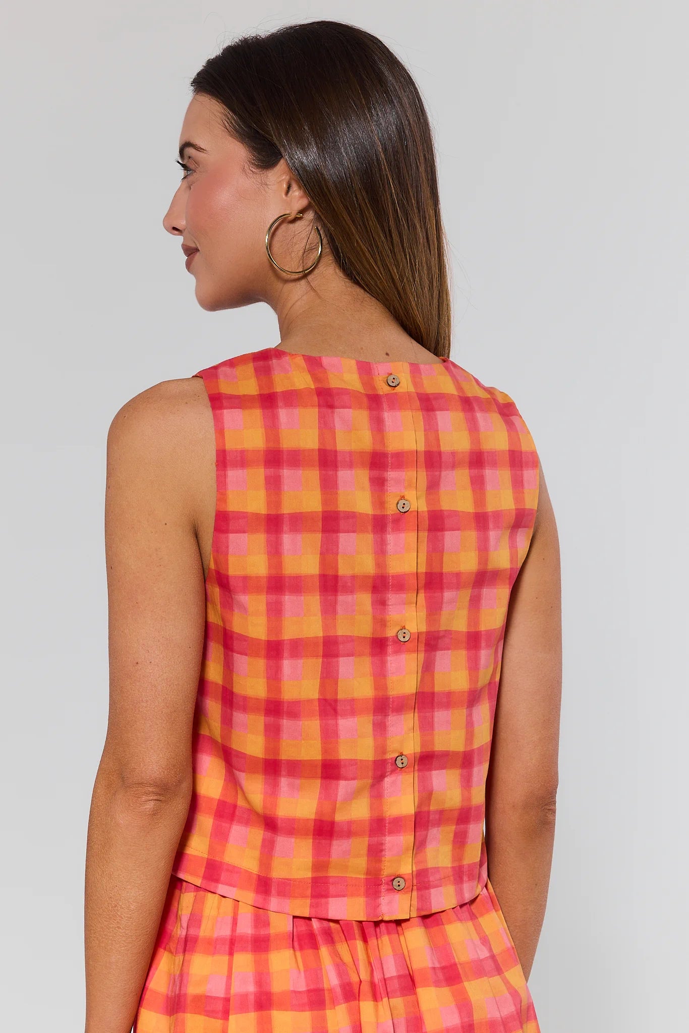 Woman wearing a sleeveless pink and yellow checkered top on a plain background