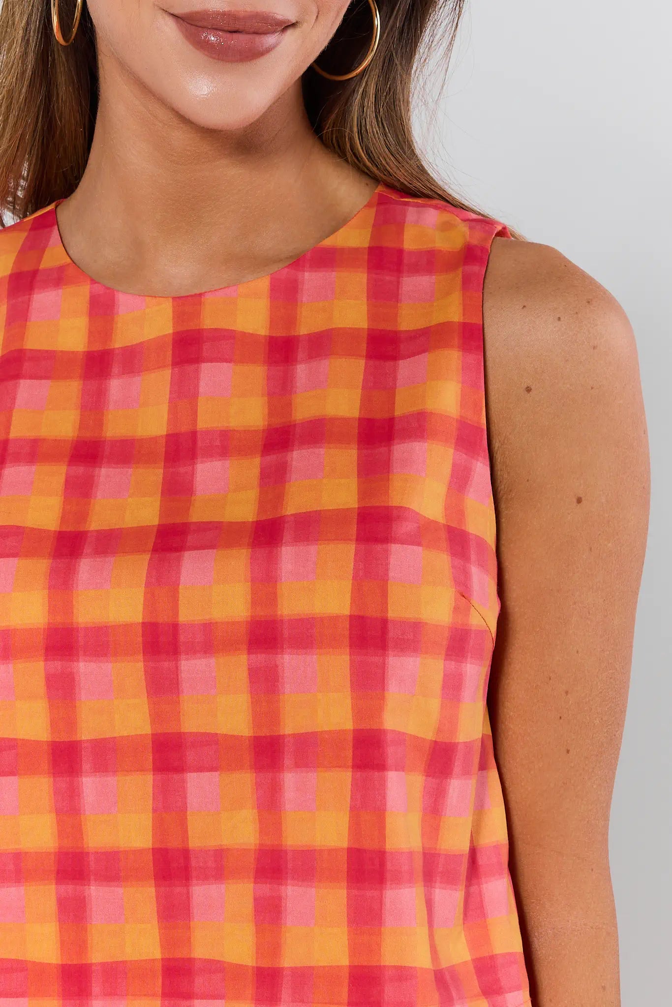 Woman wearing a sleeveless checkered dress with pink and yellow pattern on a plain background