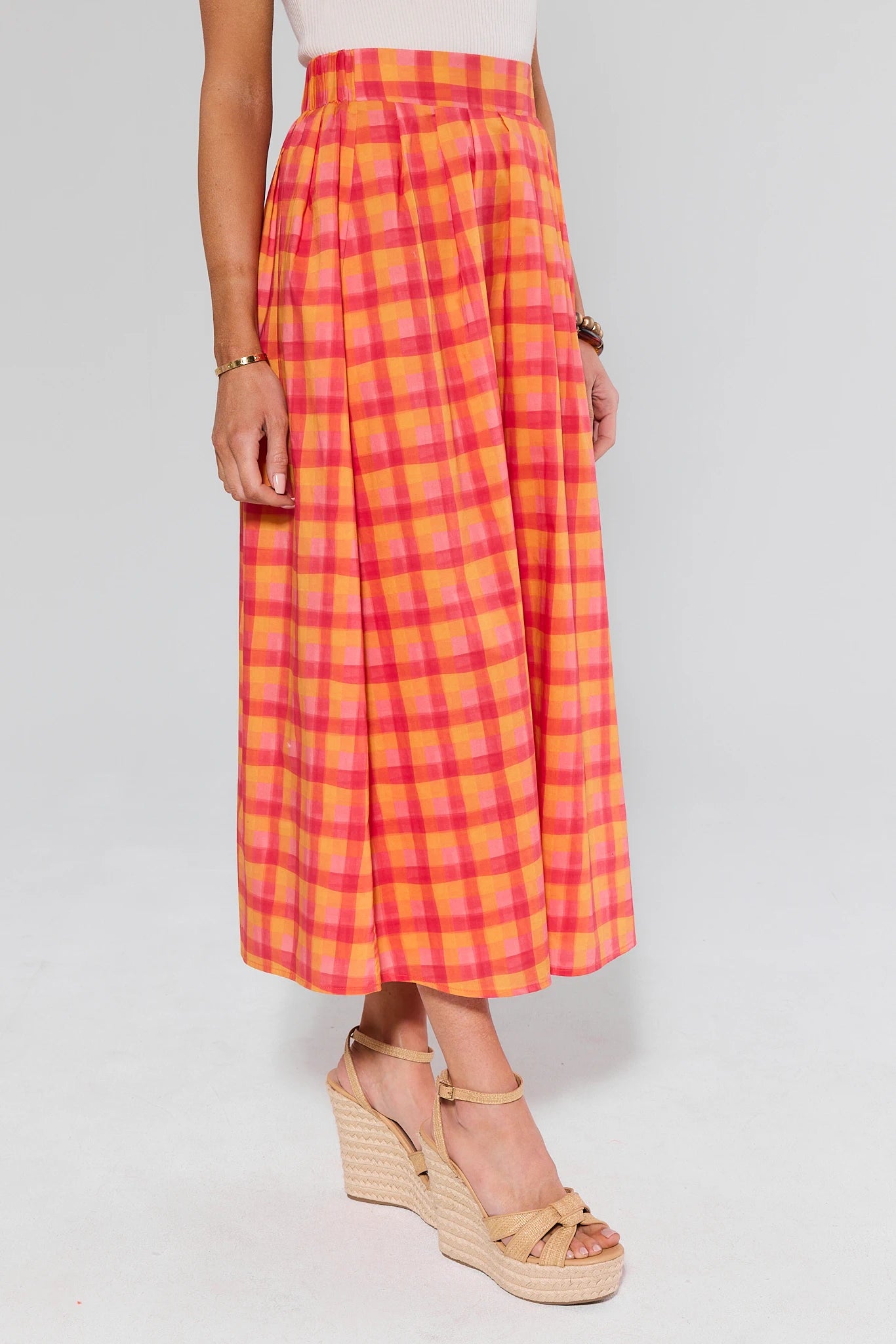 Person wearing a bright pink and orange plaid skirt on a white background