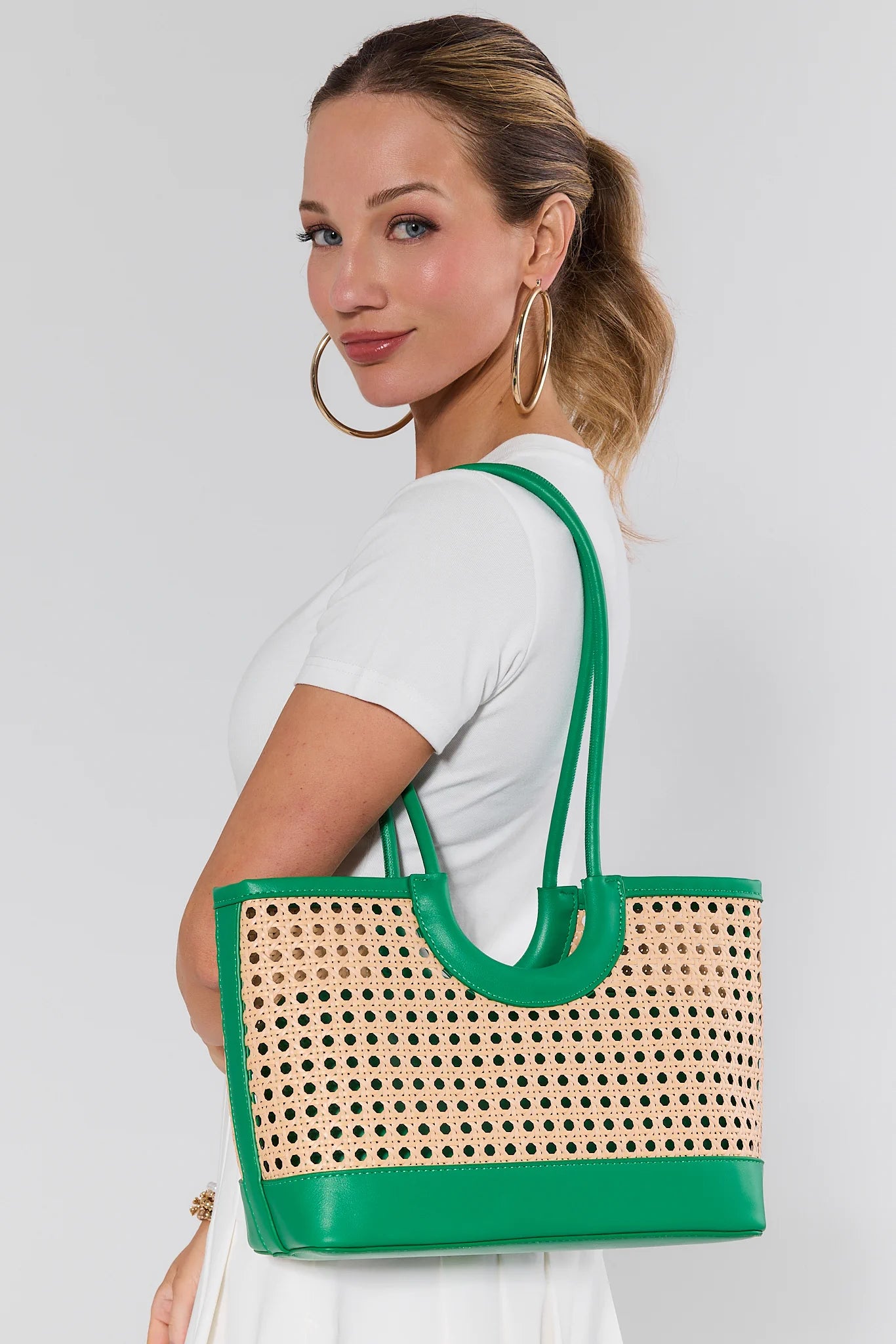 Woman holding a wicker handbag with green trim against a plain background