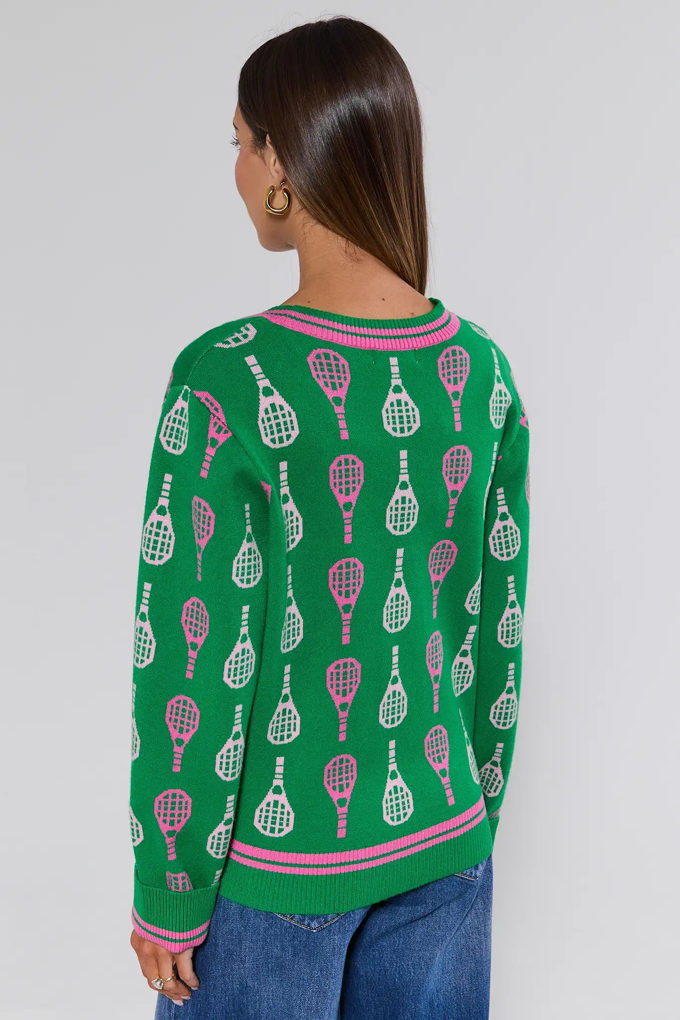 Person wearing a green sweater with tennis racket pattern on a plain background