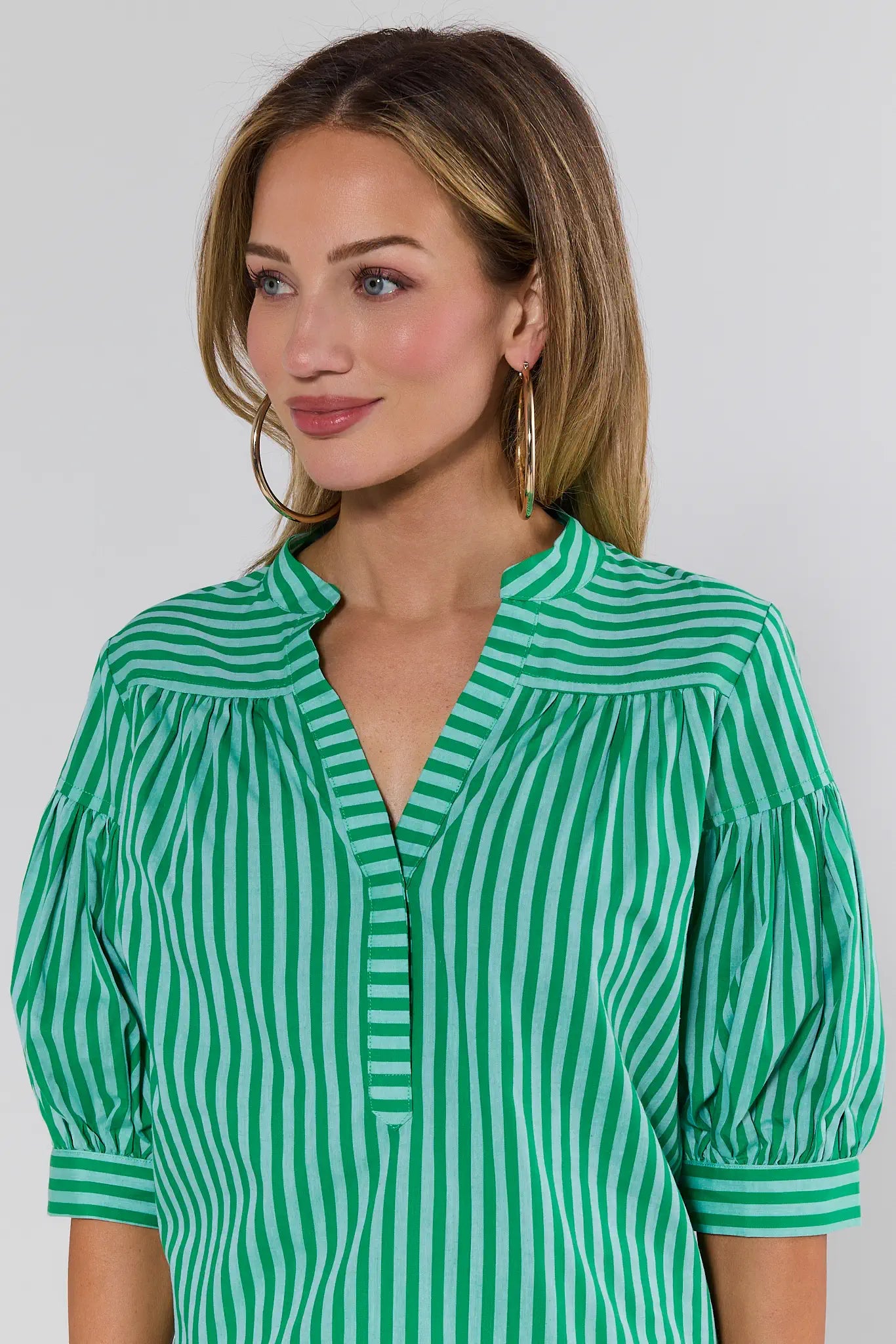 Woman wearing a green and white striped blouse against a plain background