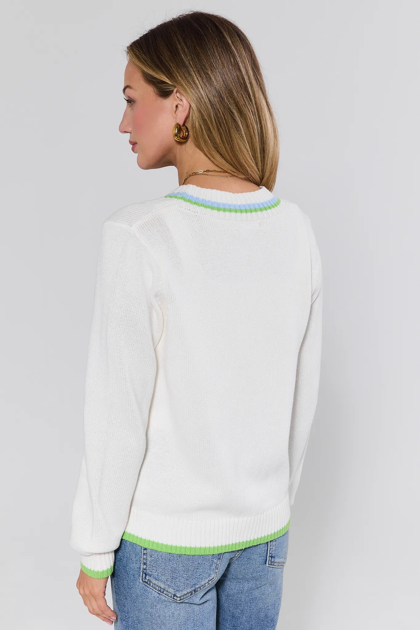 Woman wearing a white sweater with green trim on a plain background