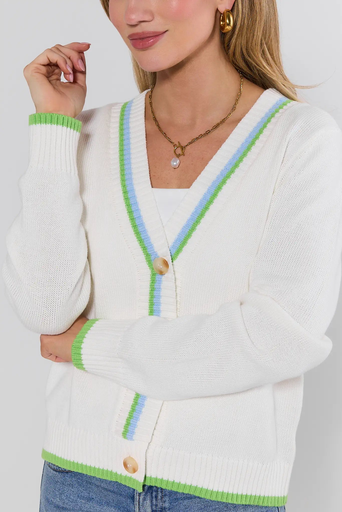 White cardigan with green and blue trim worn by a person on a white background