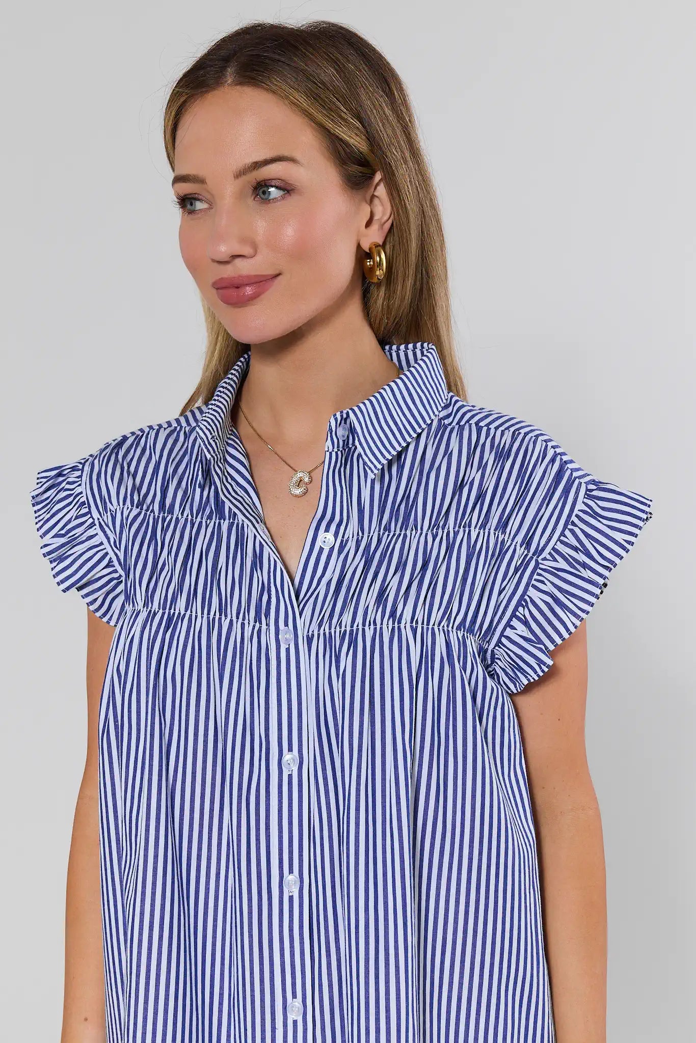 Woman wearing a blue and white striped shirt with ruffled shoulders against a gray background