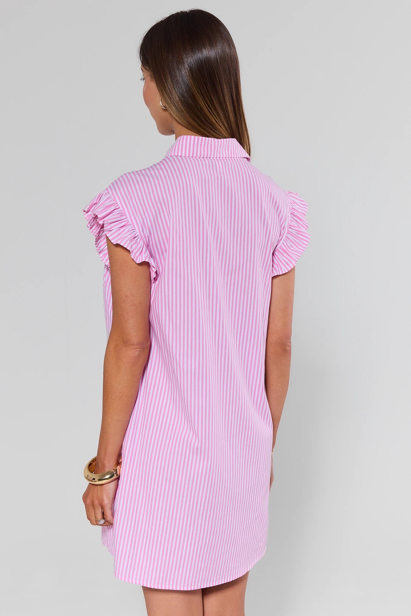 Woman wearing a pink and white striped dress with ruffled sleeves on a plain background