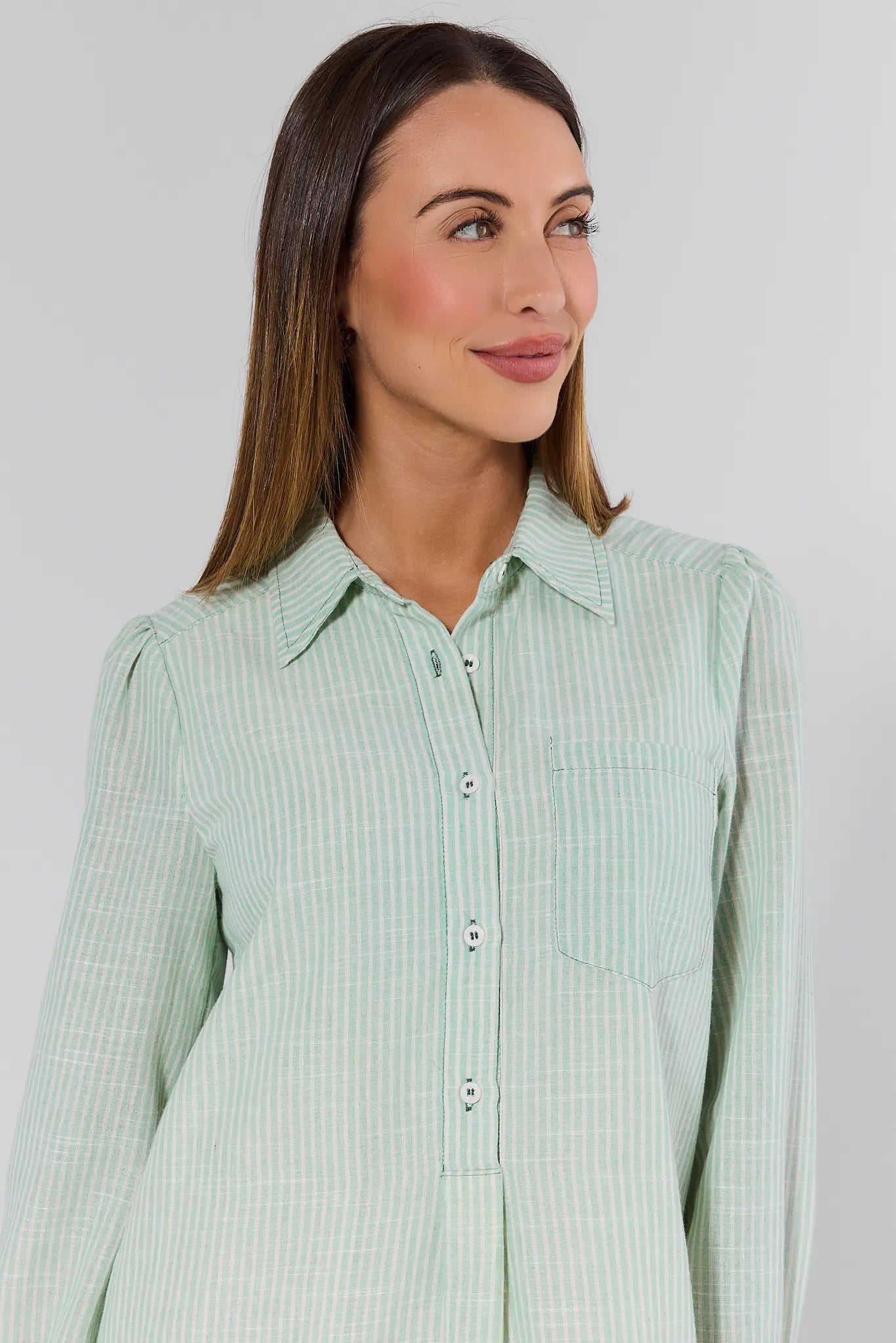 Woman wearing a light green checkered shirt against a plain background