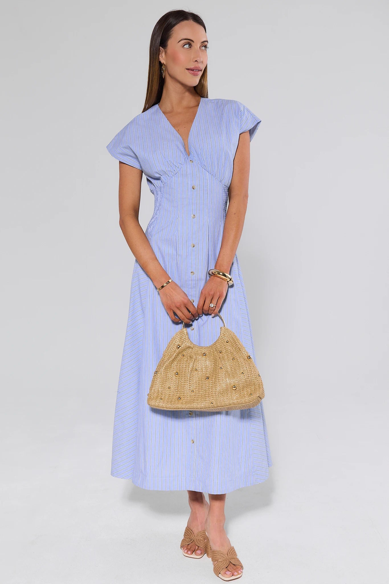 Woman wearing a light blue dress holding a woven bag on a white background