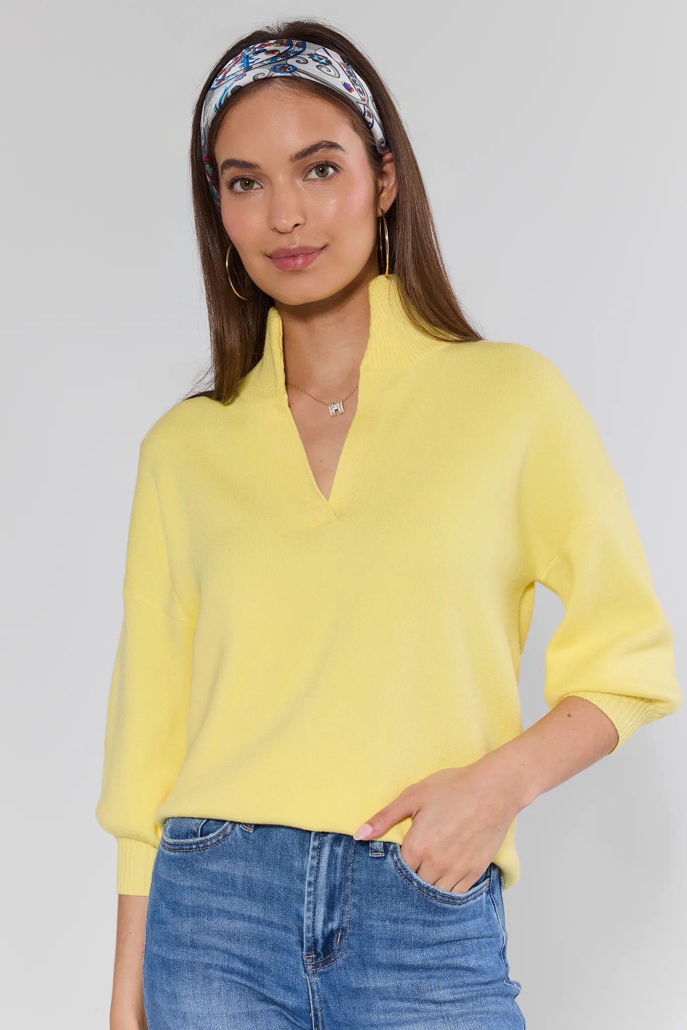 Woman wearing a yellow sweater and blue jeans with a white background