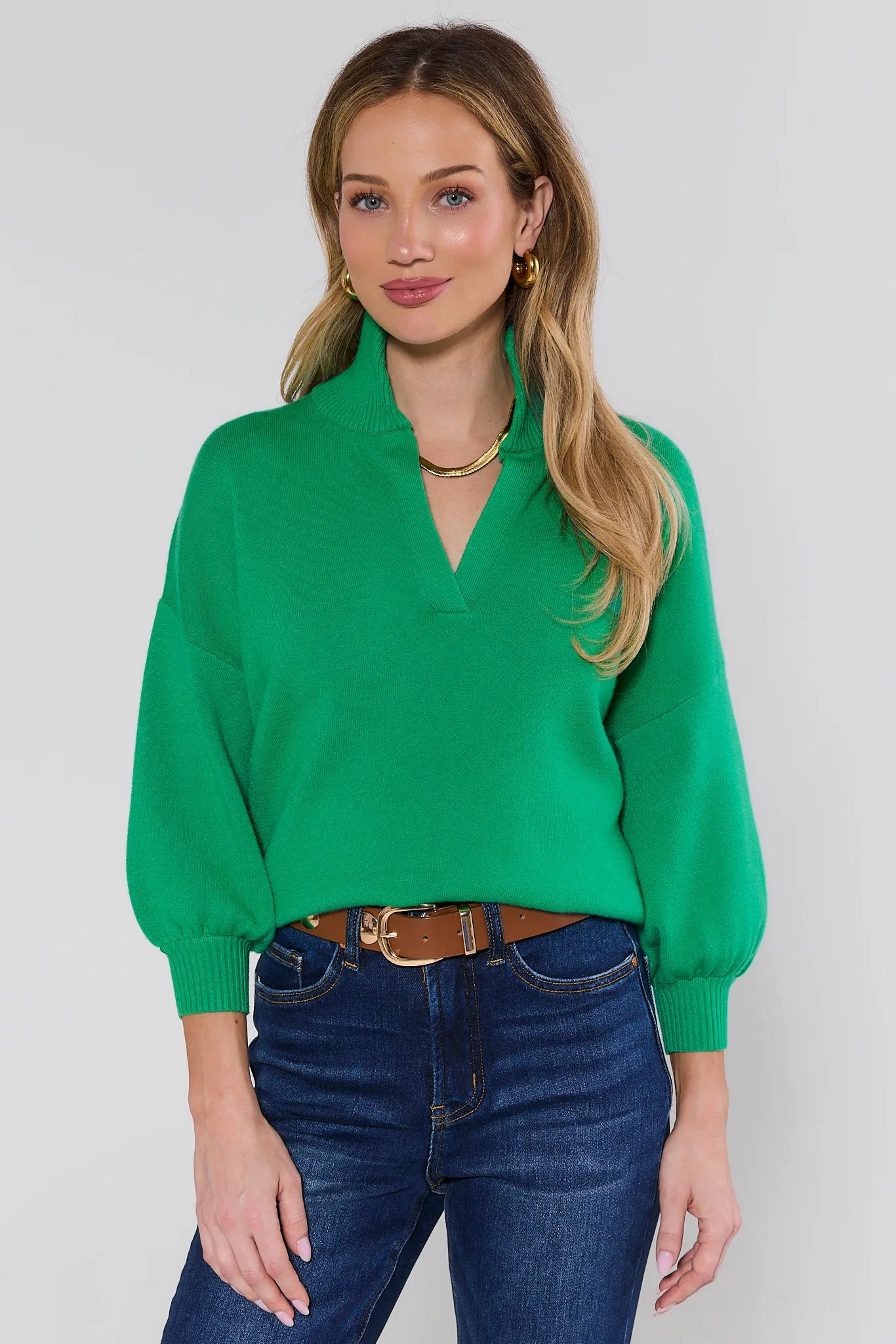 Woman wearing a green sweater and blue jeans against a white background