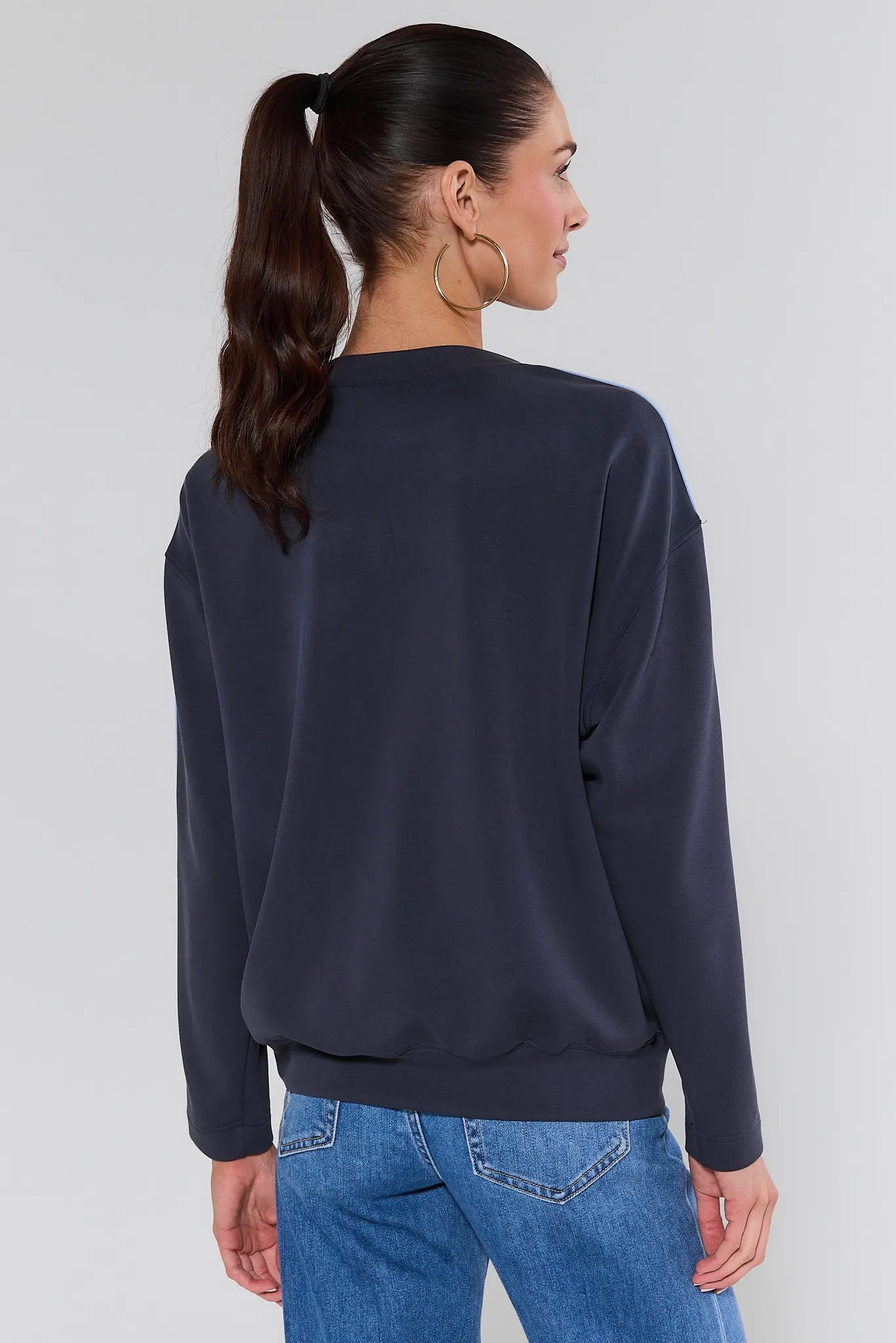Woman wearing a navy sweater and blue jeans against a white background