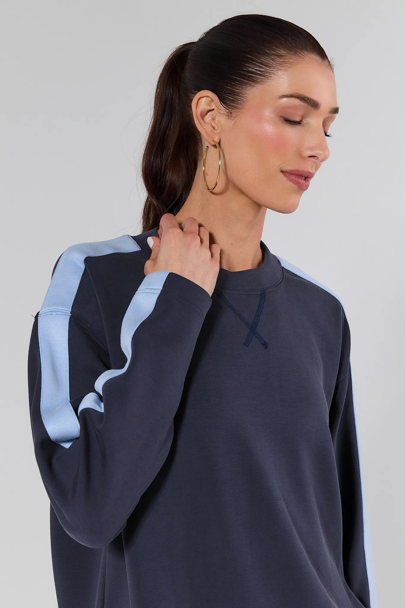 Woman wearing a navy sweatshirt with light blue sleeves against a plain background