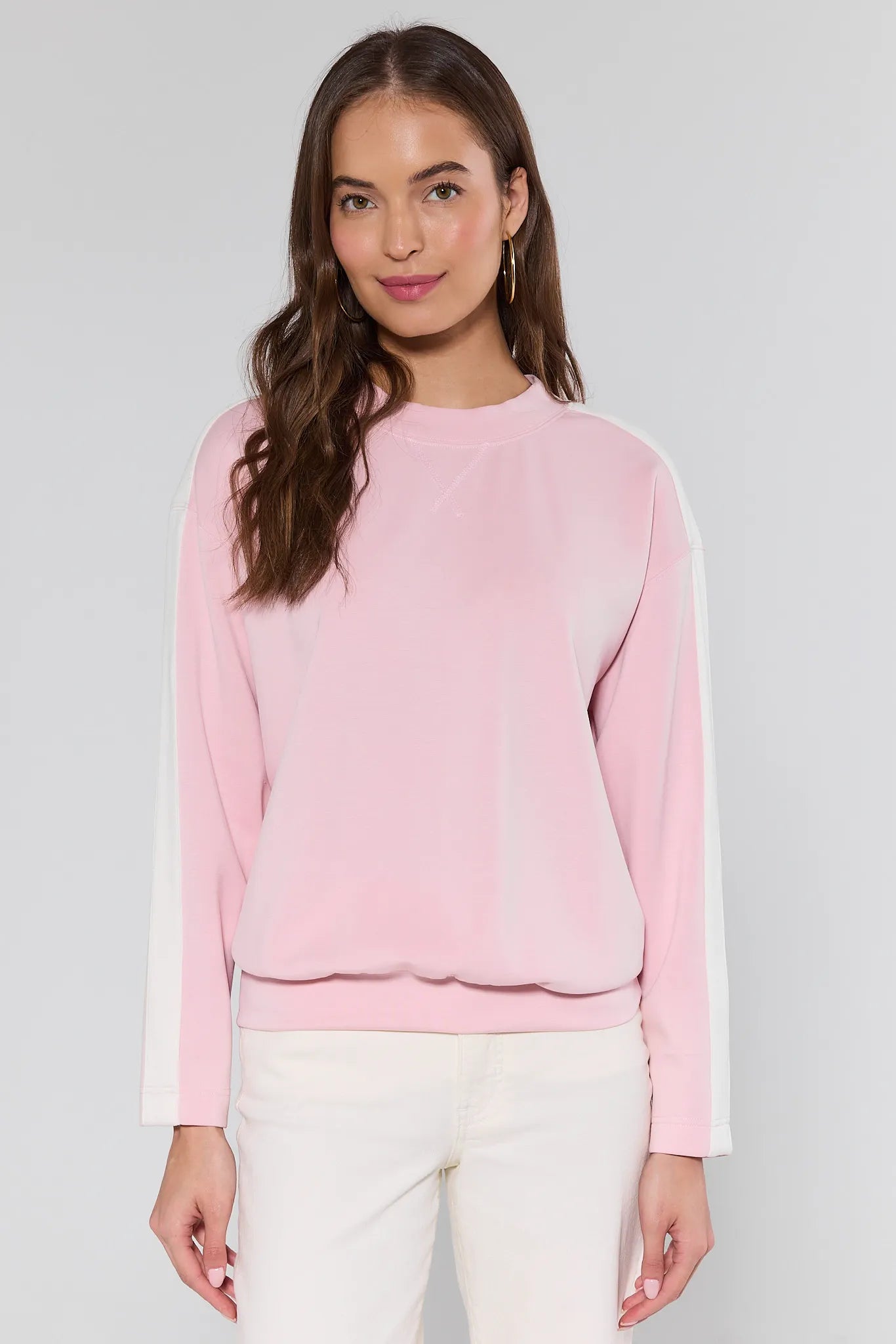 Woman wearing a pink sweater with white trim on a plain background