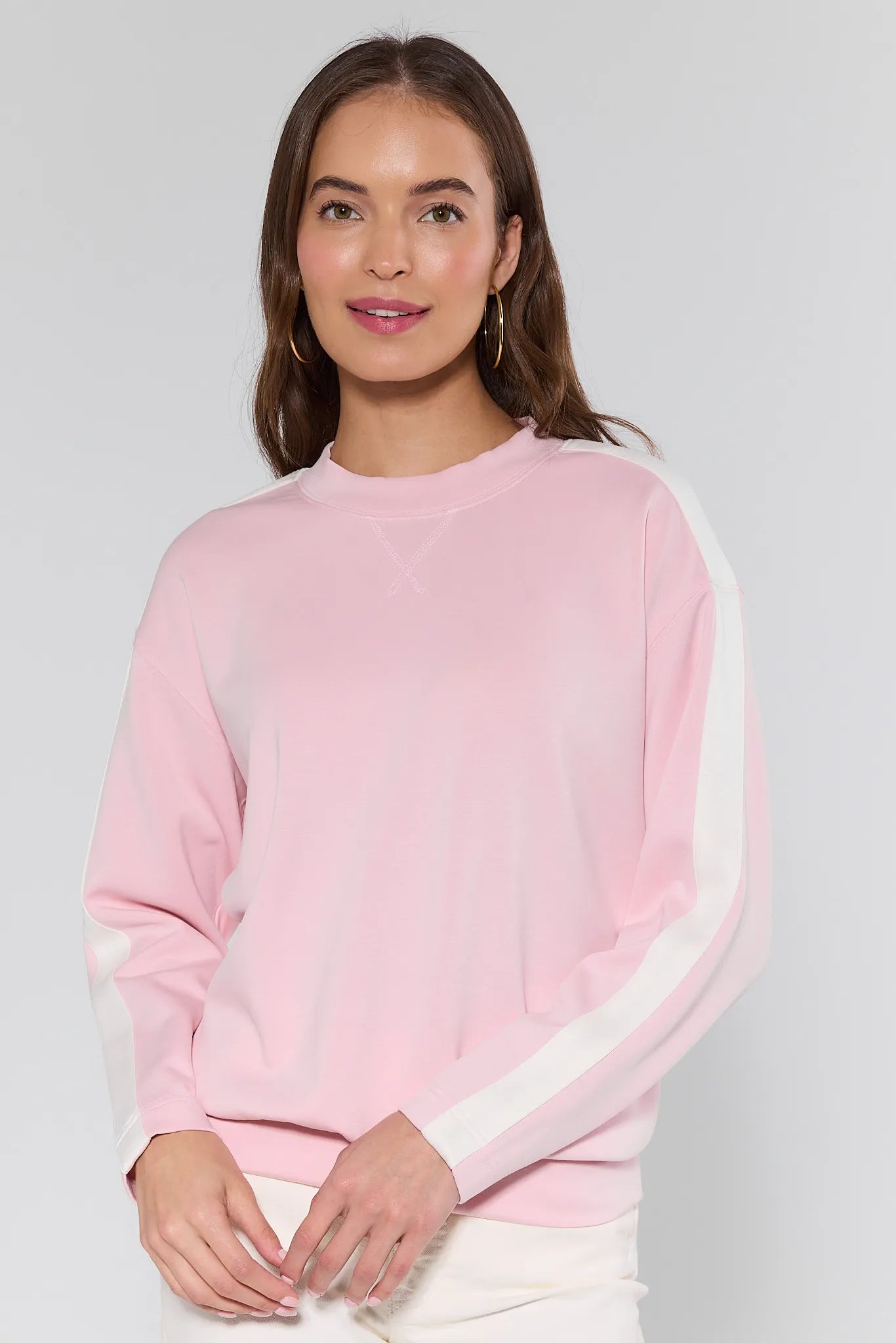 Woman wearing a pink sweater with white sleeves against a plain background
