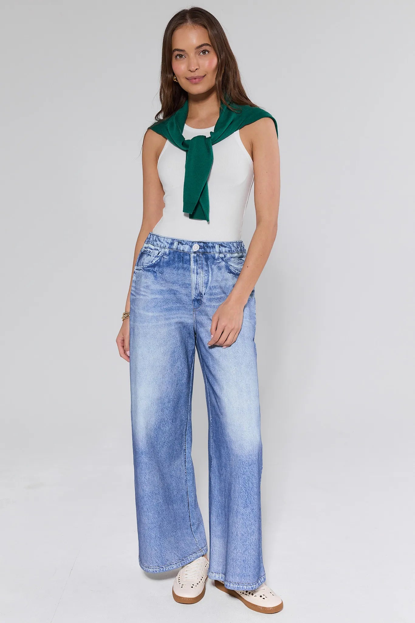 Woman wearing a white top with a green scarf and blue jeans on a plain background