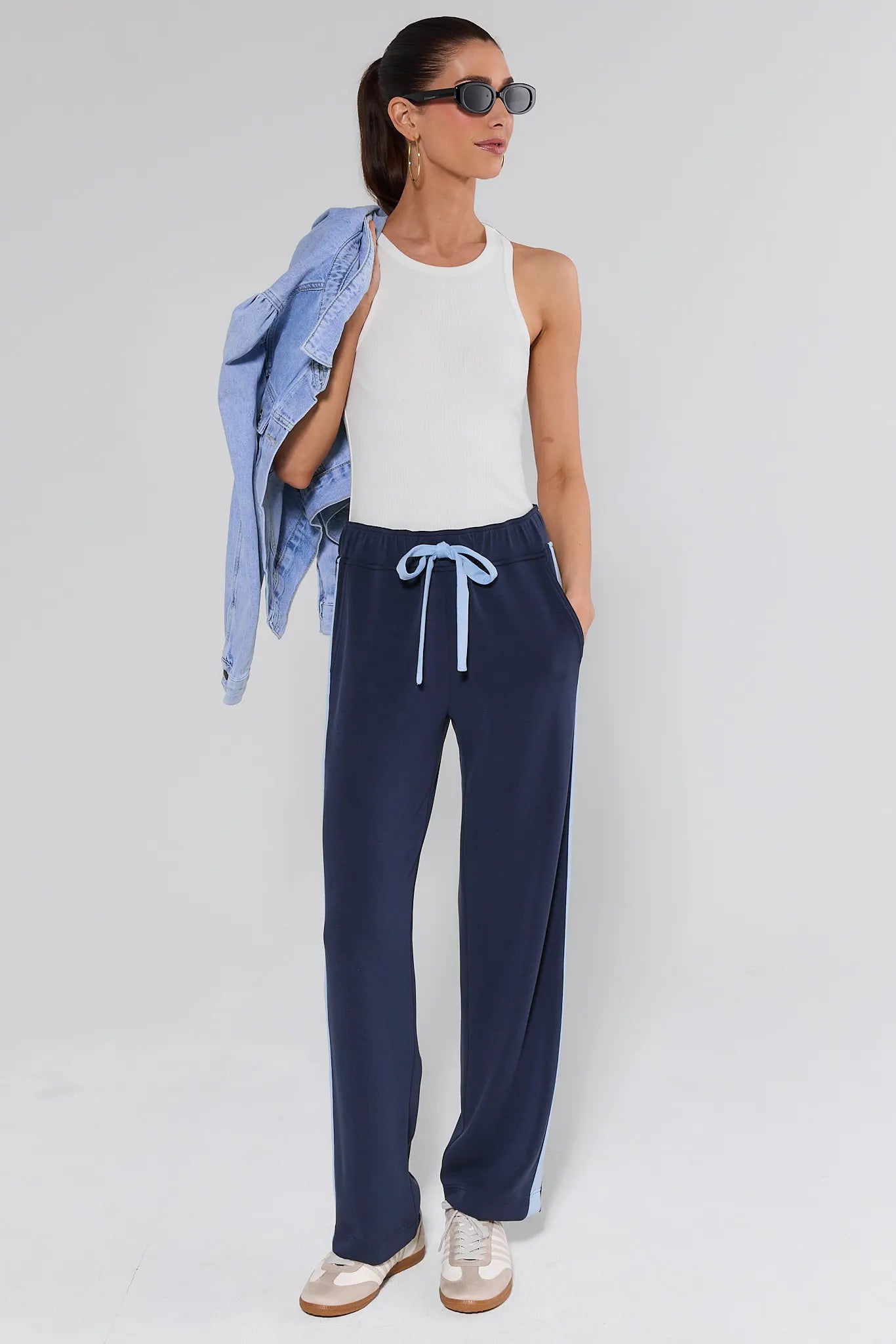 Woman wearing navy pants with a white top and blue jacket on a light gray background