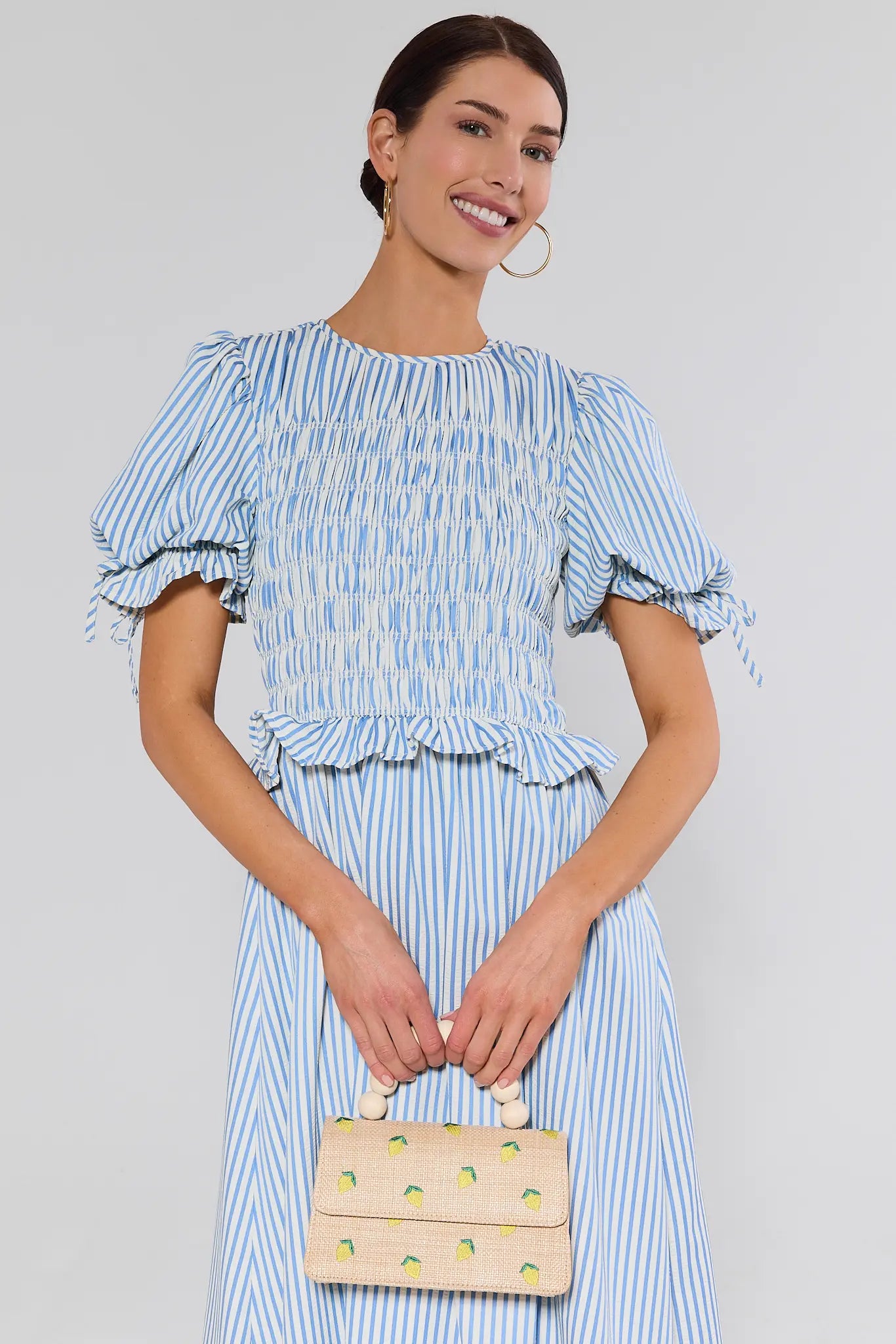 Woman wearing a blue and white striped dress holding a matching handbag against a plain background