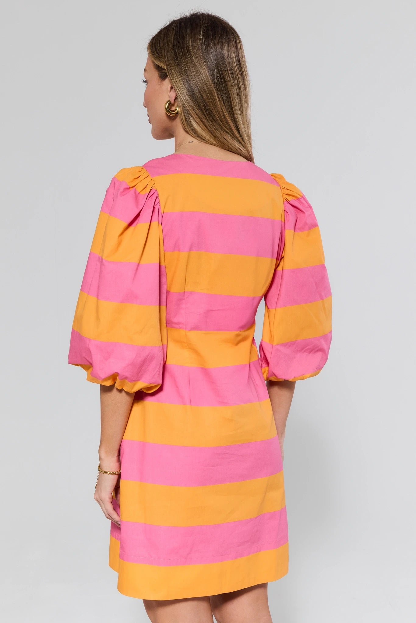 Woman wearing a pink and orange striped dress against a plain background