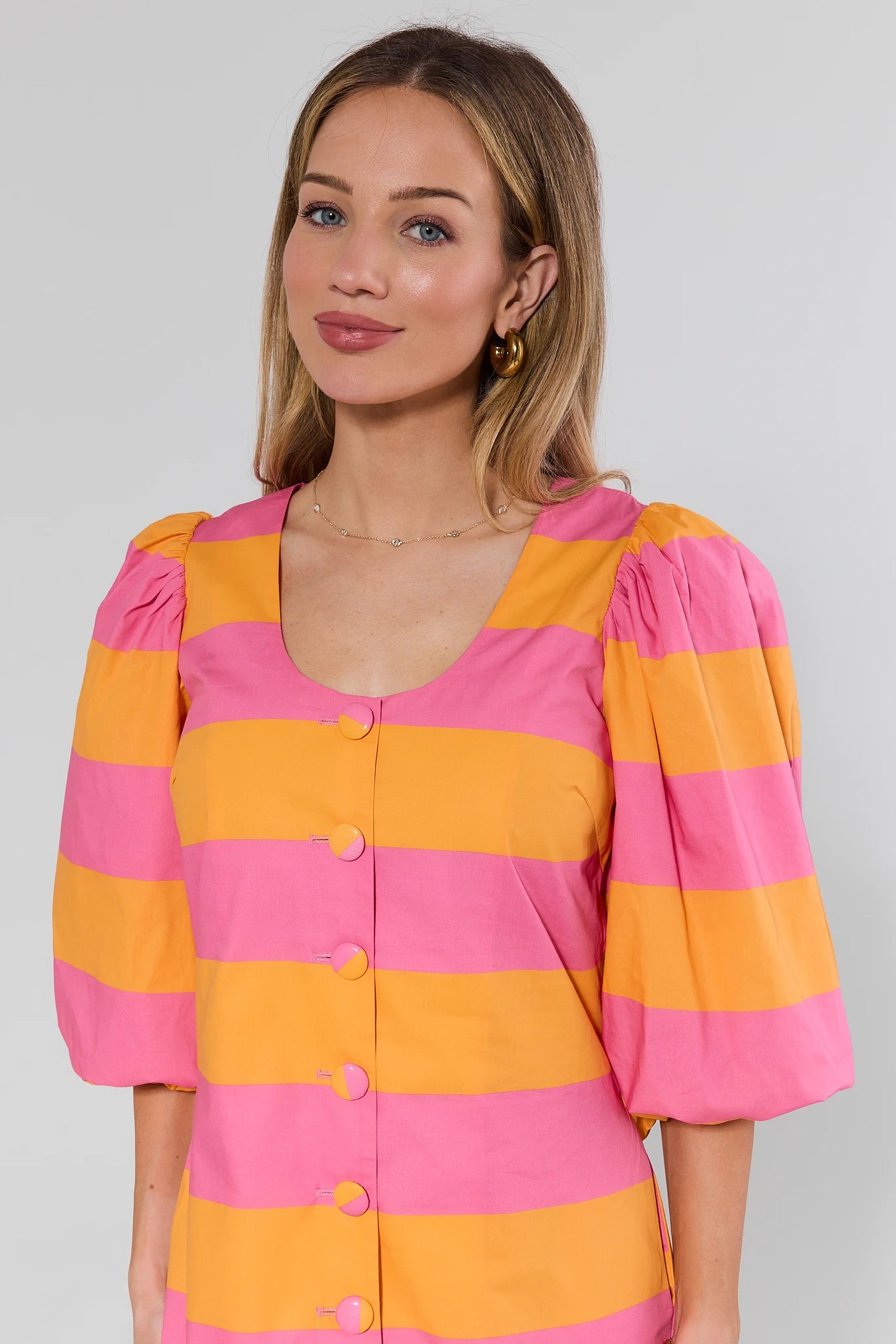 Woman wearing a pink and orange striped dress against a plain background