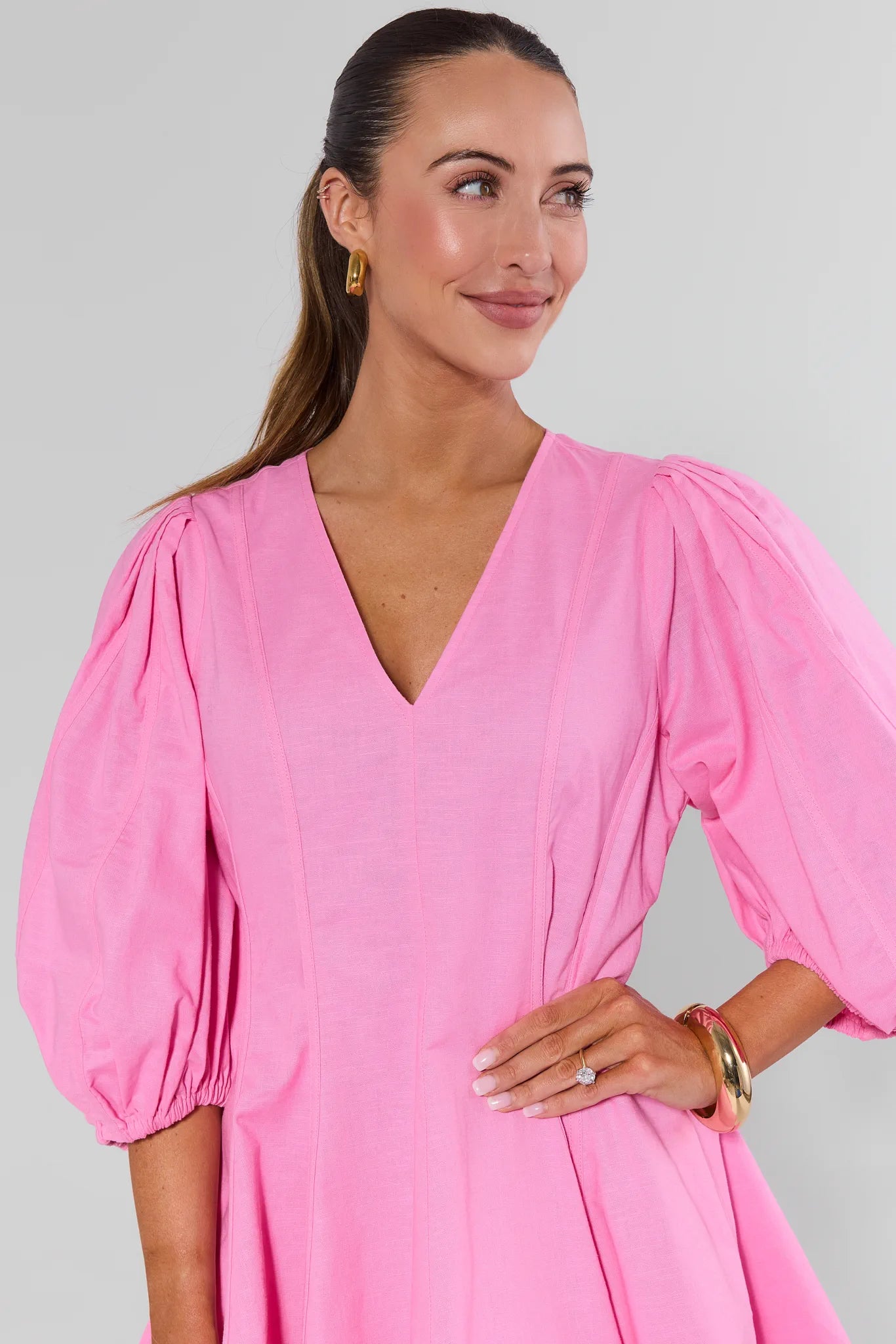 Woman wearing a pink dress with puffed sleeves against a gray background