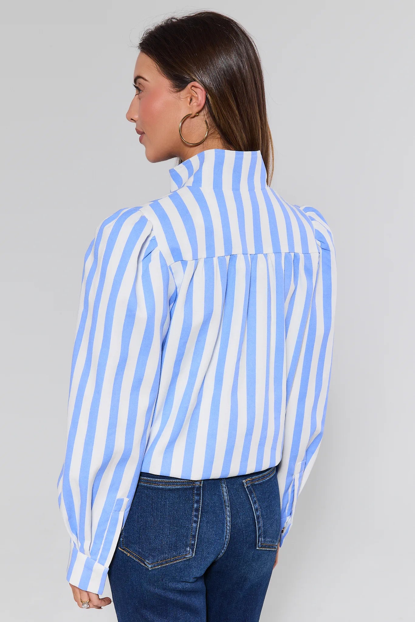 Woman wearing a blue and white striped shirt and jeans against a gray background