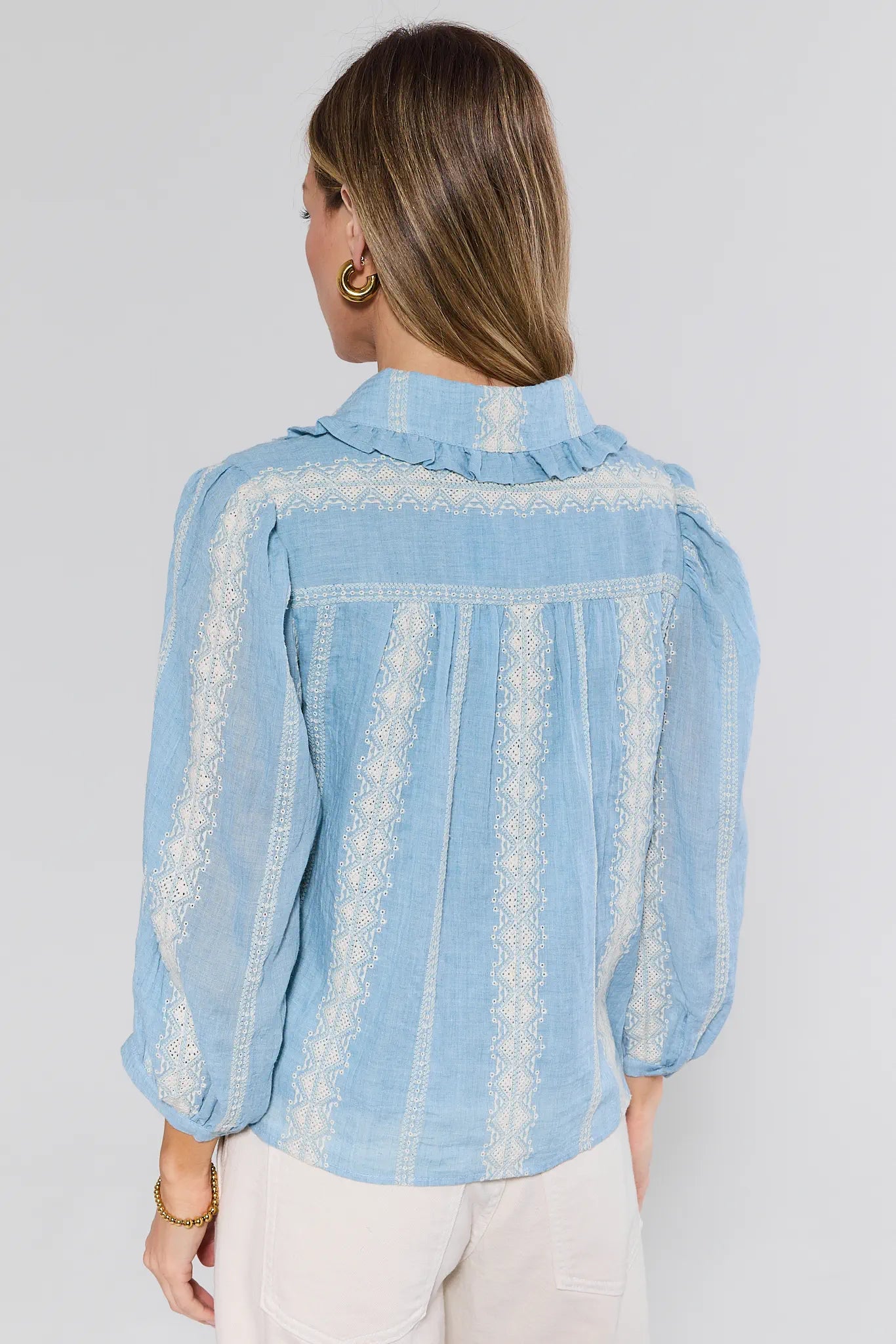 Woman wearing a light blue denim shirt with lace details on a plain background