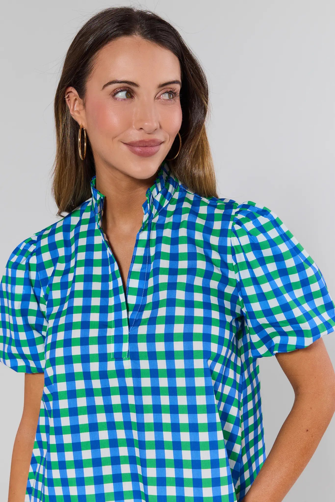 Woman wearing Kathleen Mixed Gingham Short Sleeve Top with a gingham pattern, small standing collar, puff sleeves, and V-neck, set against a light-gray background.