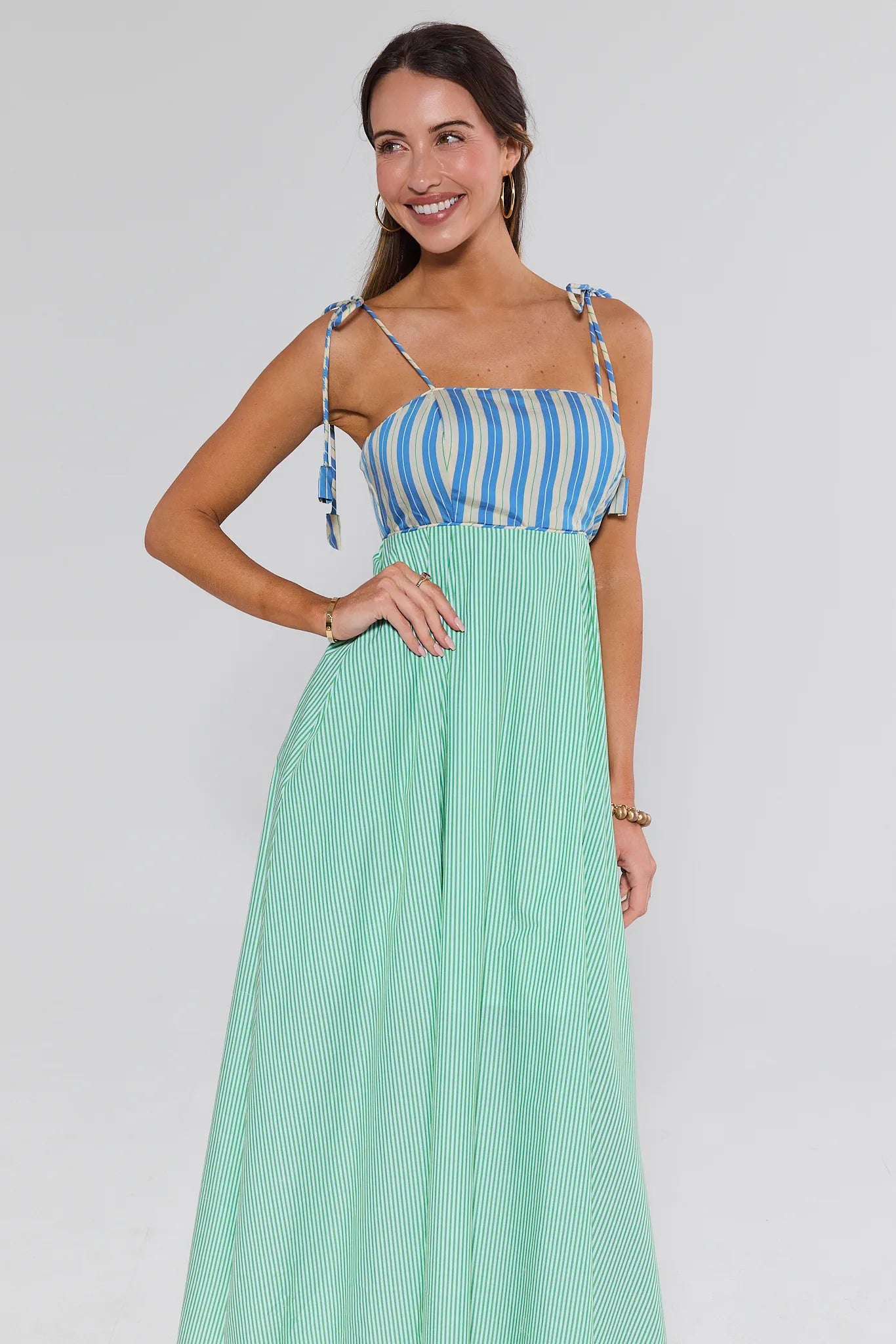 Woman wearing a blue and white striped top with a green pleated skirt on a plain background