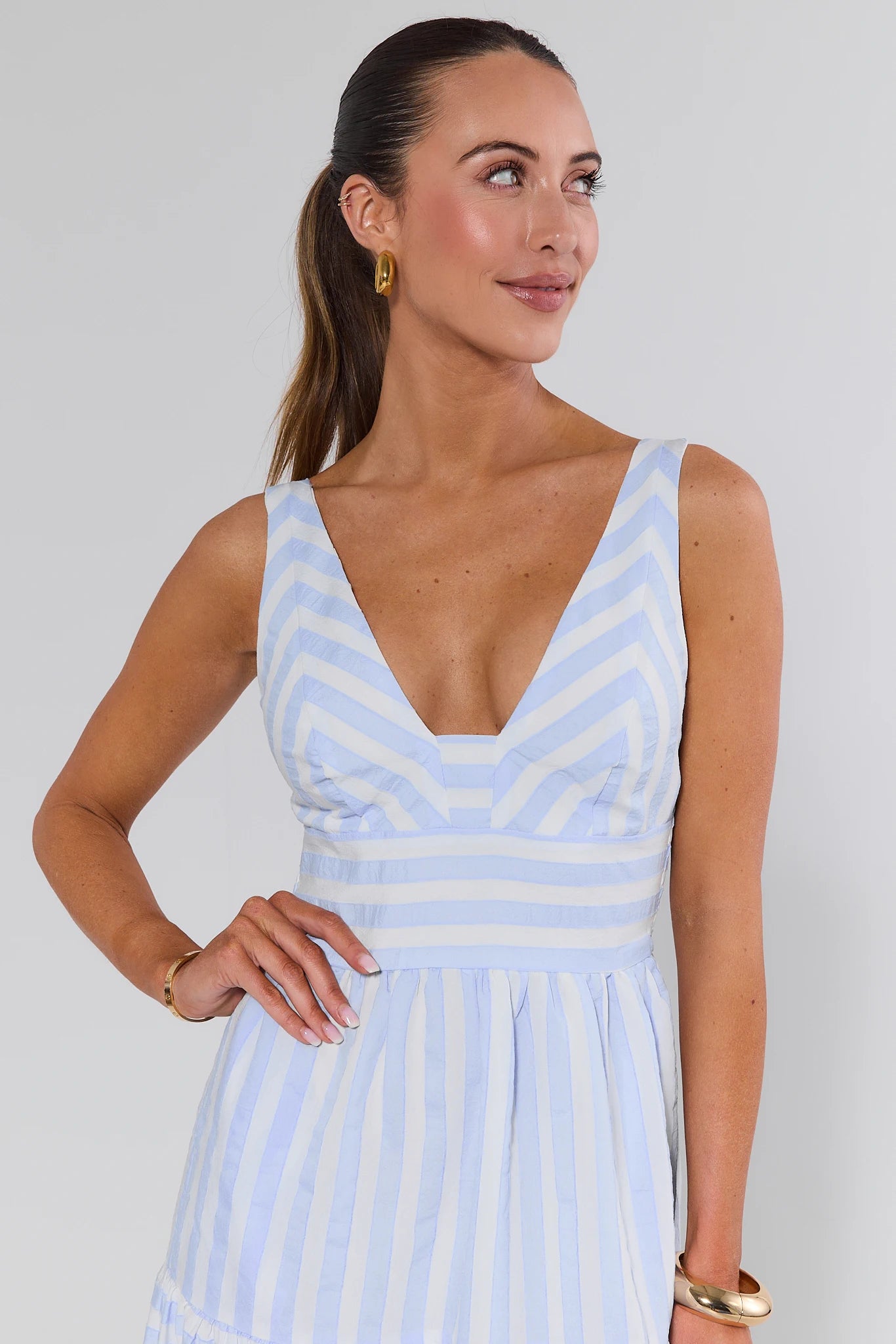 Woman wearing a light blue and white striped dress against a plain background