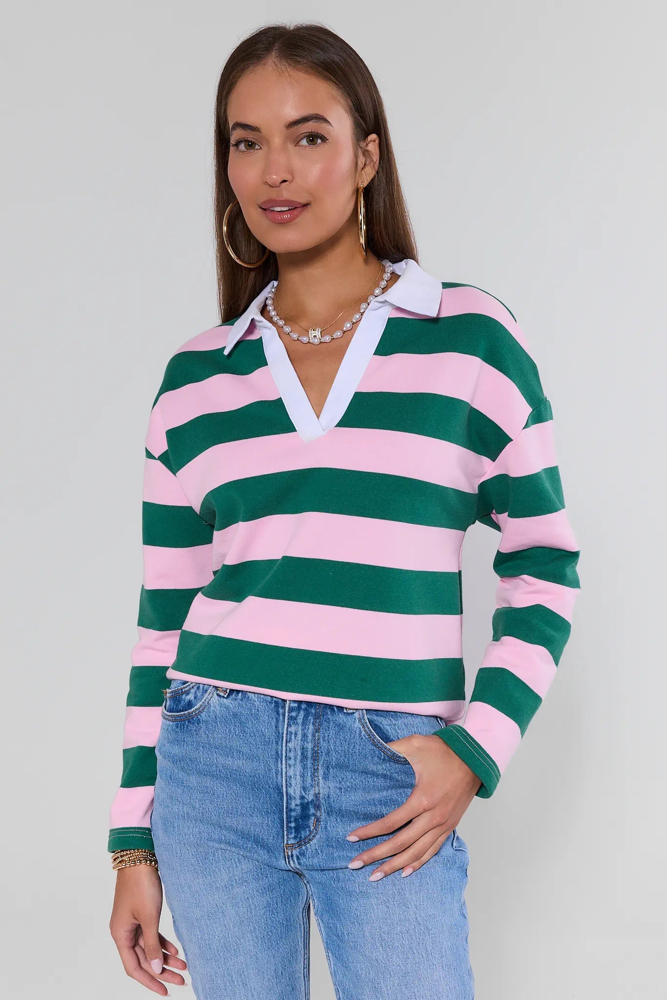 Woman wearing a green and pink striped sweater with blue jeans against a plain background