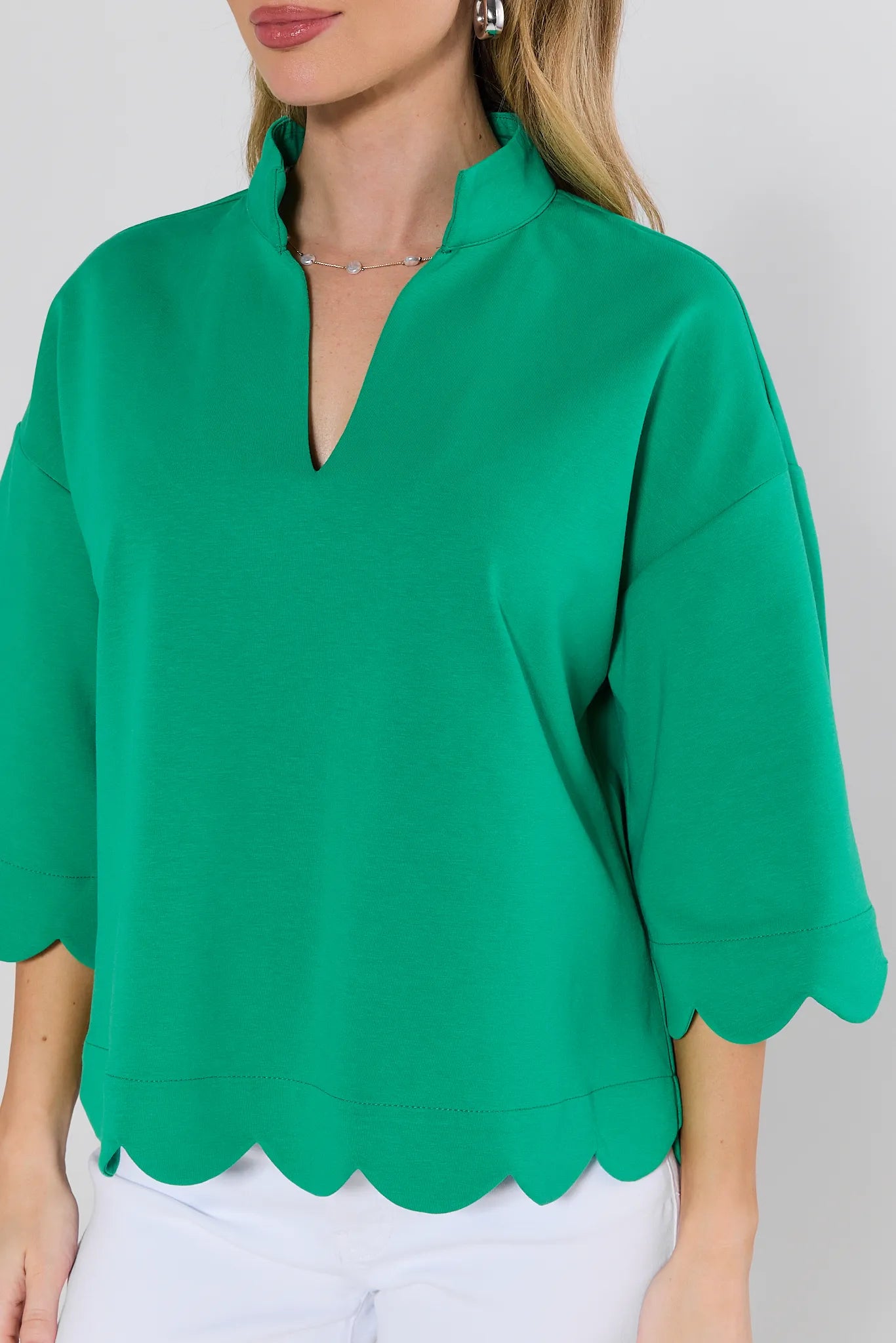 Green blouse with scalloped hem worn by a person on a plain background