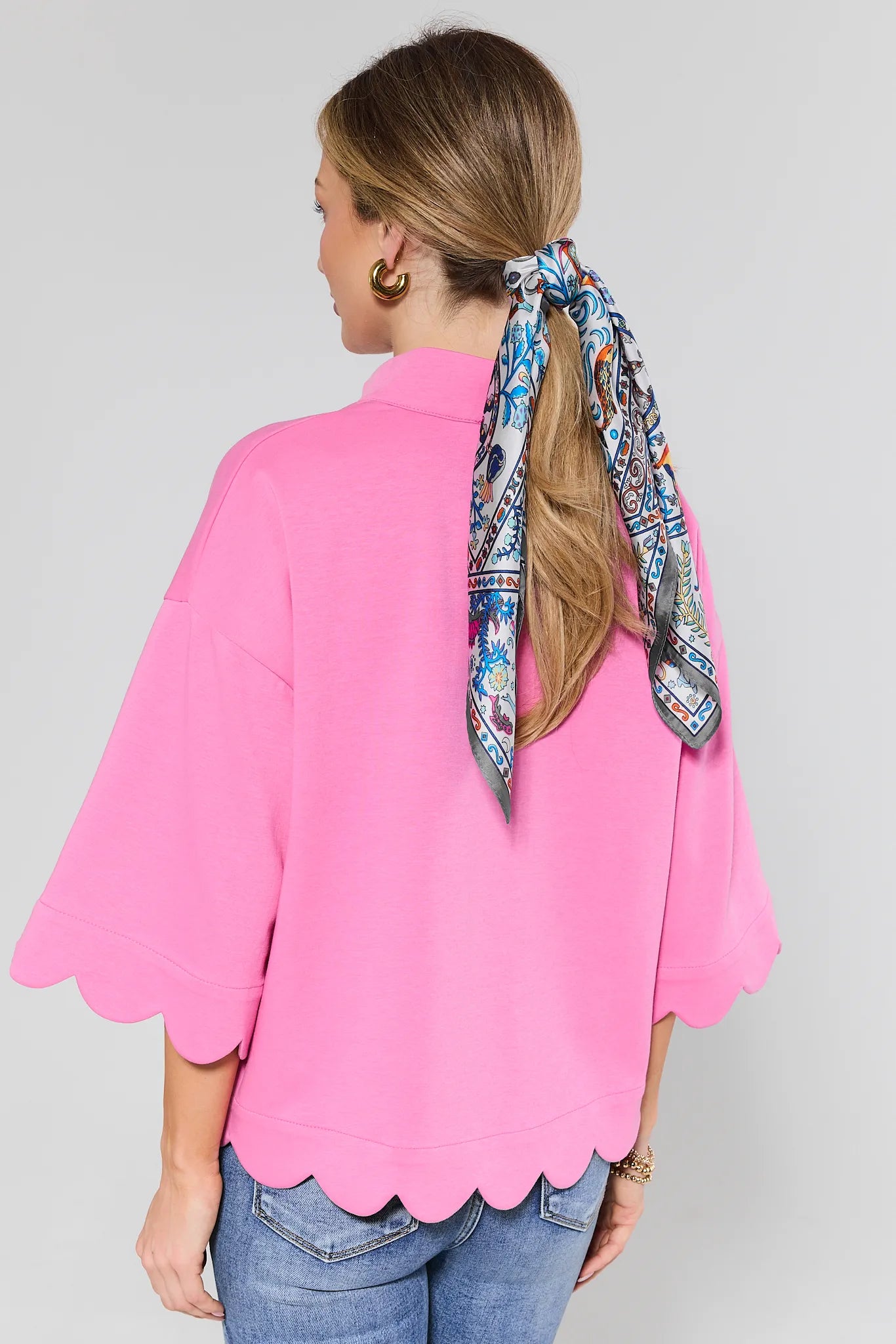 Woman wearing a pink blouse with a floral scarf tied around her head on a plain background