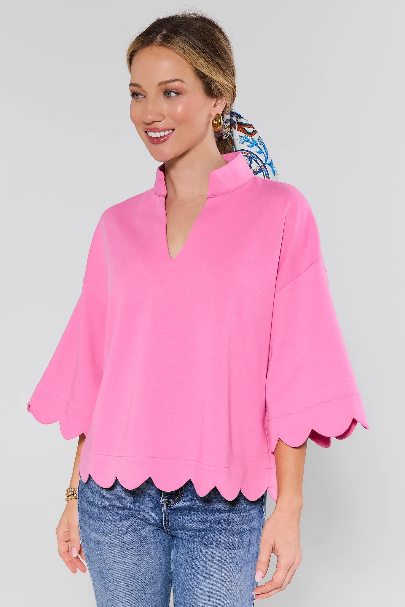 Woman wearing a pink blouse with scalloped edges and blue jeans on a plain background