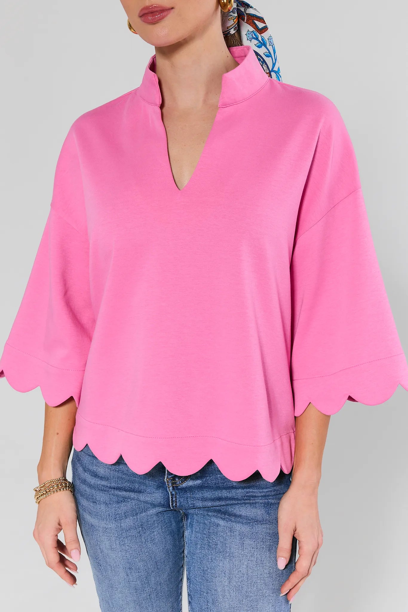 Pink blouse with scalloped hem and blue jeans on a plain background