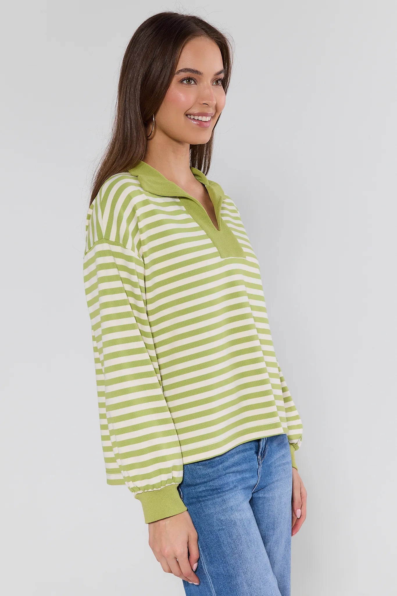 woman wearing green sweater with stripes and hoop earrings on white background