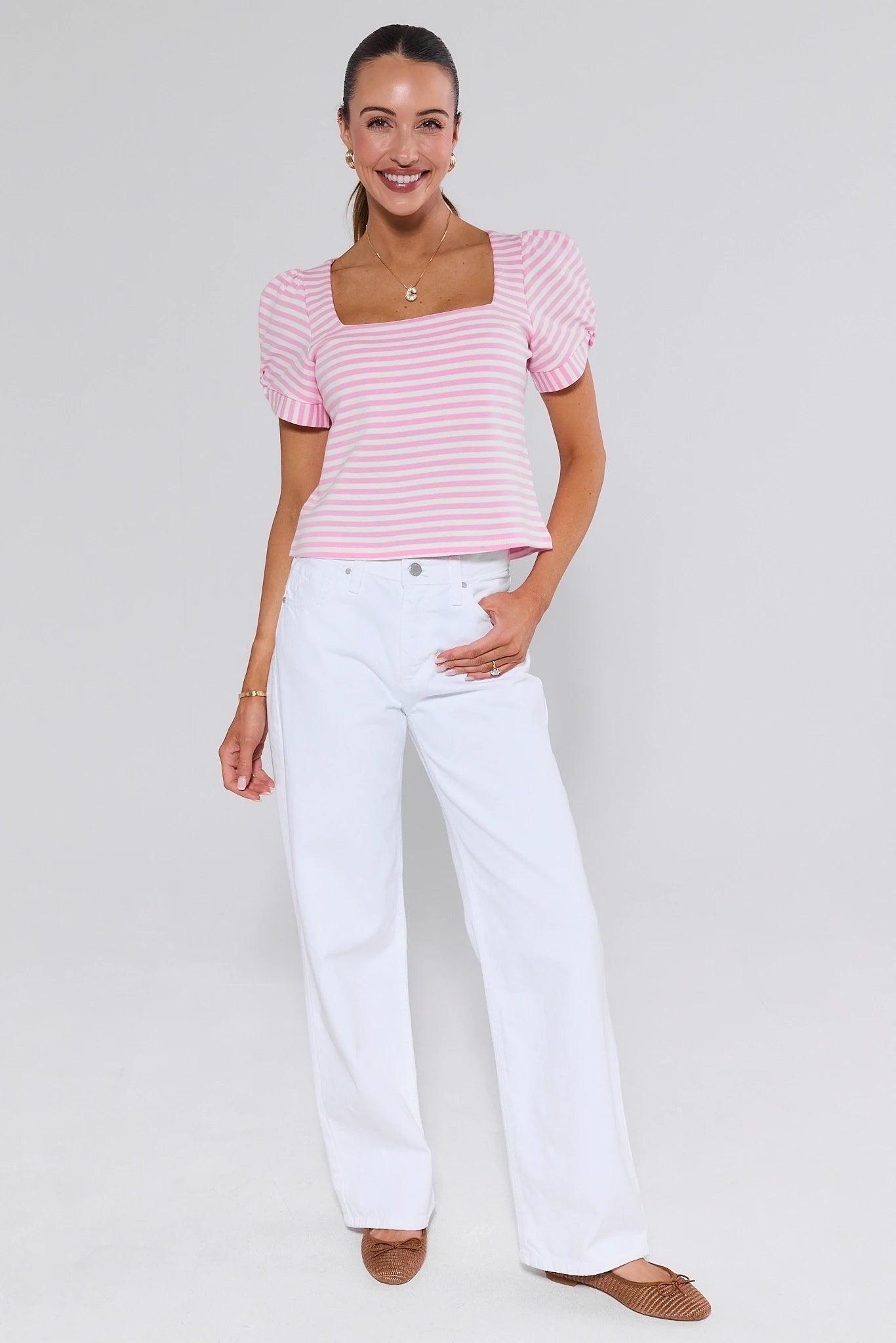 Woman wearing a pink and white striped top and white pants on a plain background