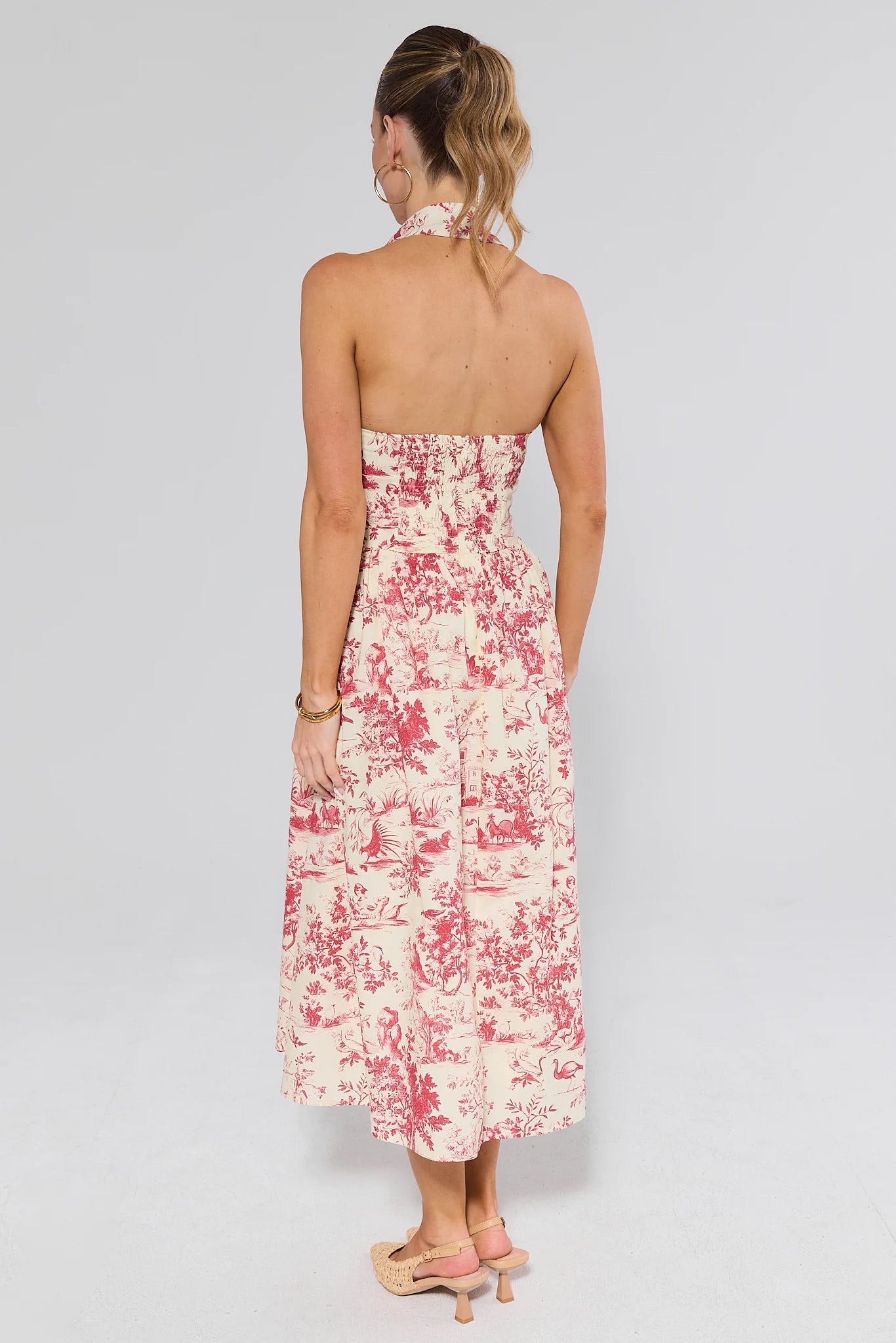 Woman standing wearing a halter floral dress on a plain background