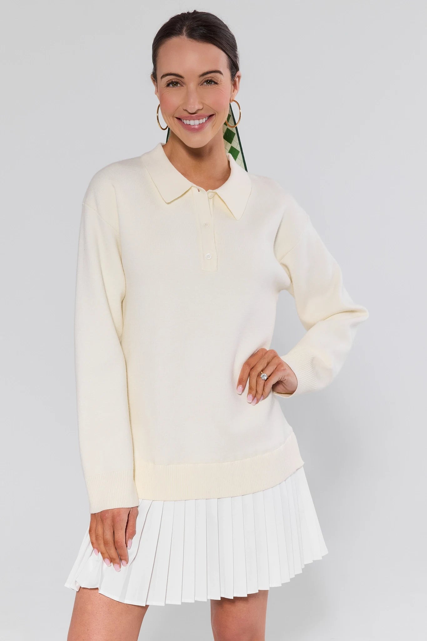 Woman wearing a light yellow sweater and white pleated skirt on a plain background