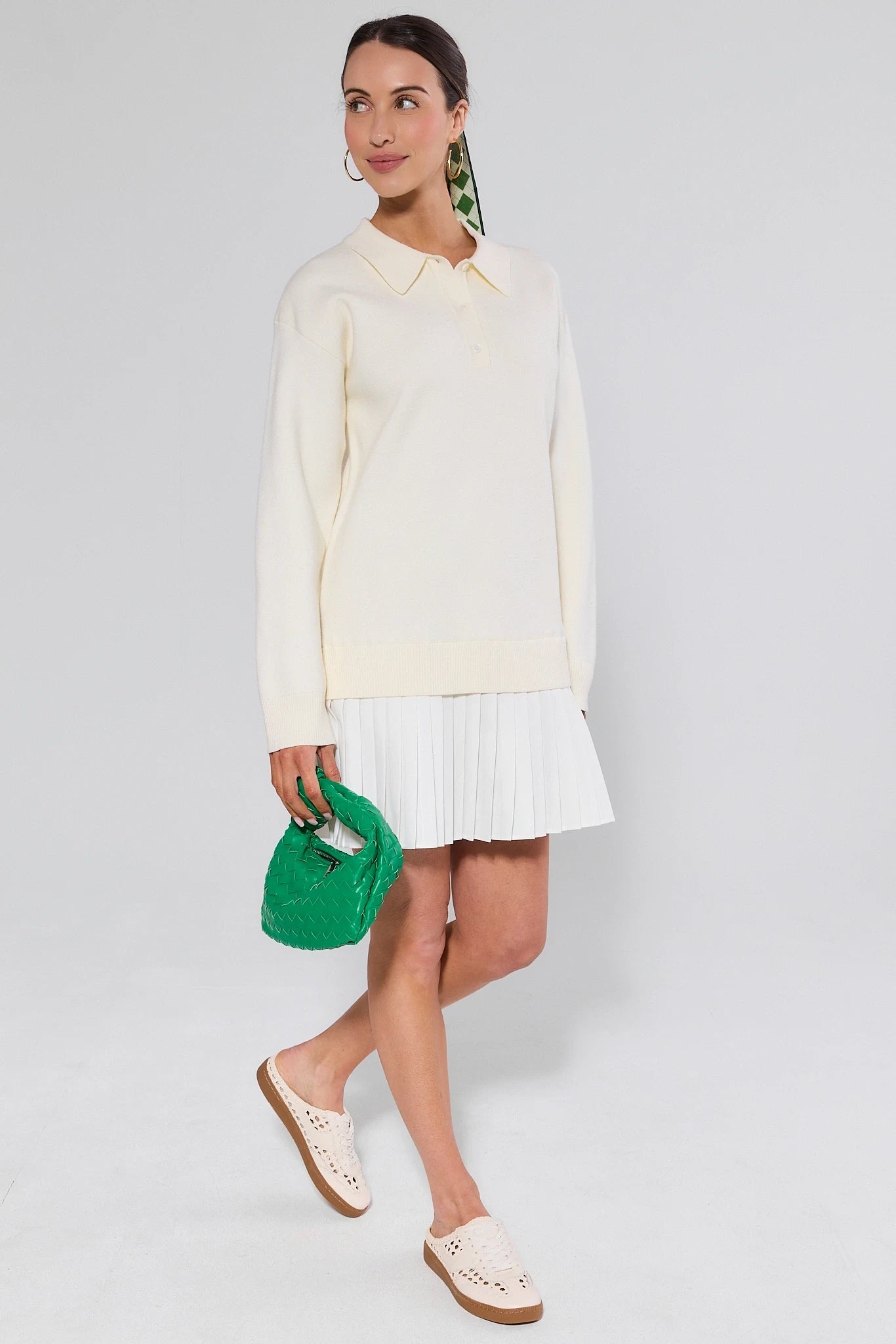 Woman wearing a light-colored blouse and white skirt, holding a green clutch against a plain background