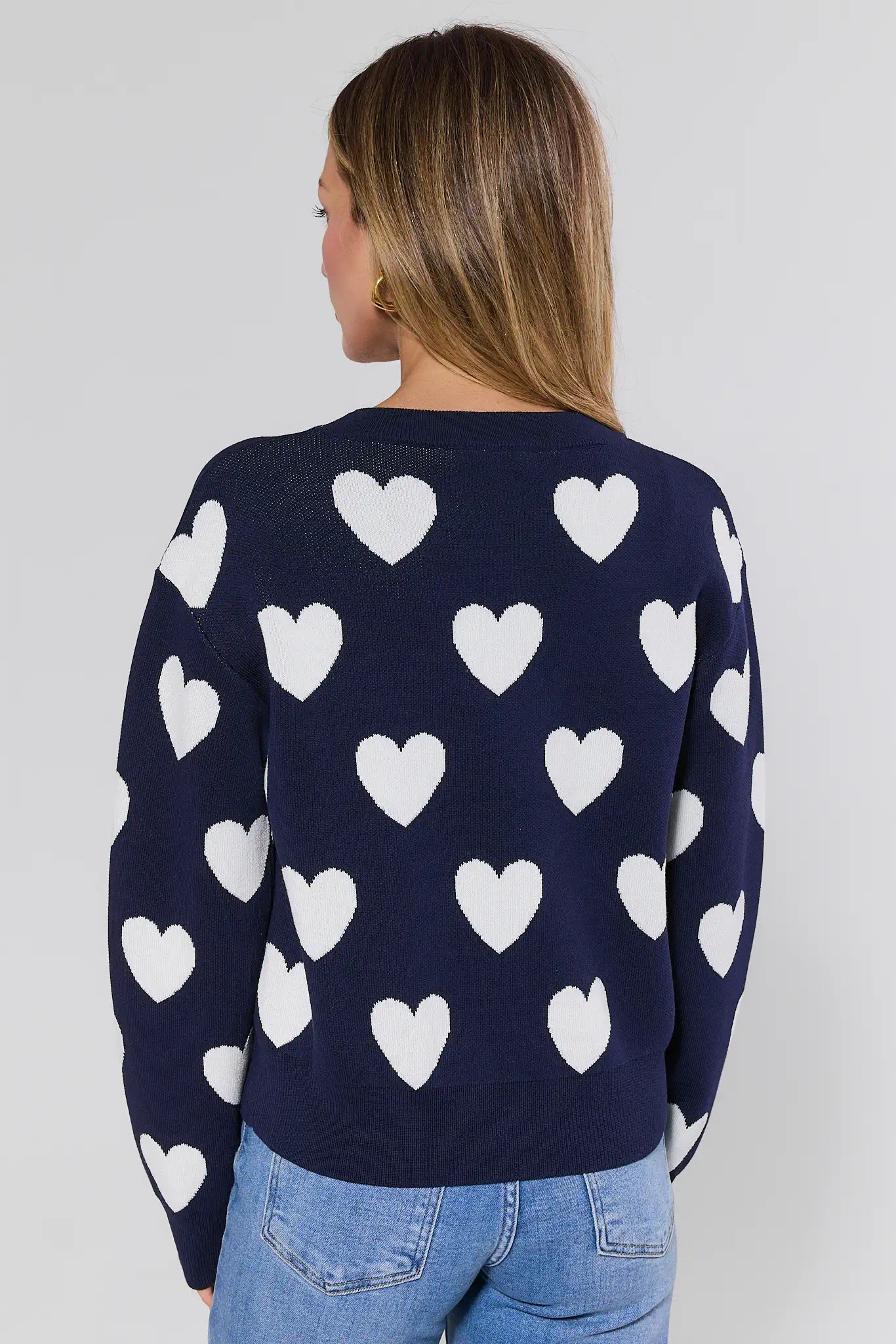 Navy sweater with white heart patterns worn by a person on a plain background