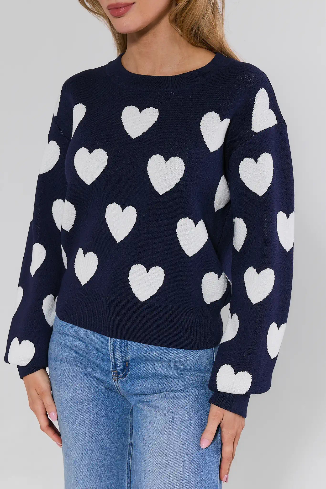 Navy sweater with white heart patterns worn by a person on a plain background