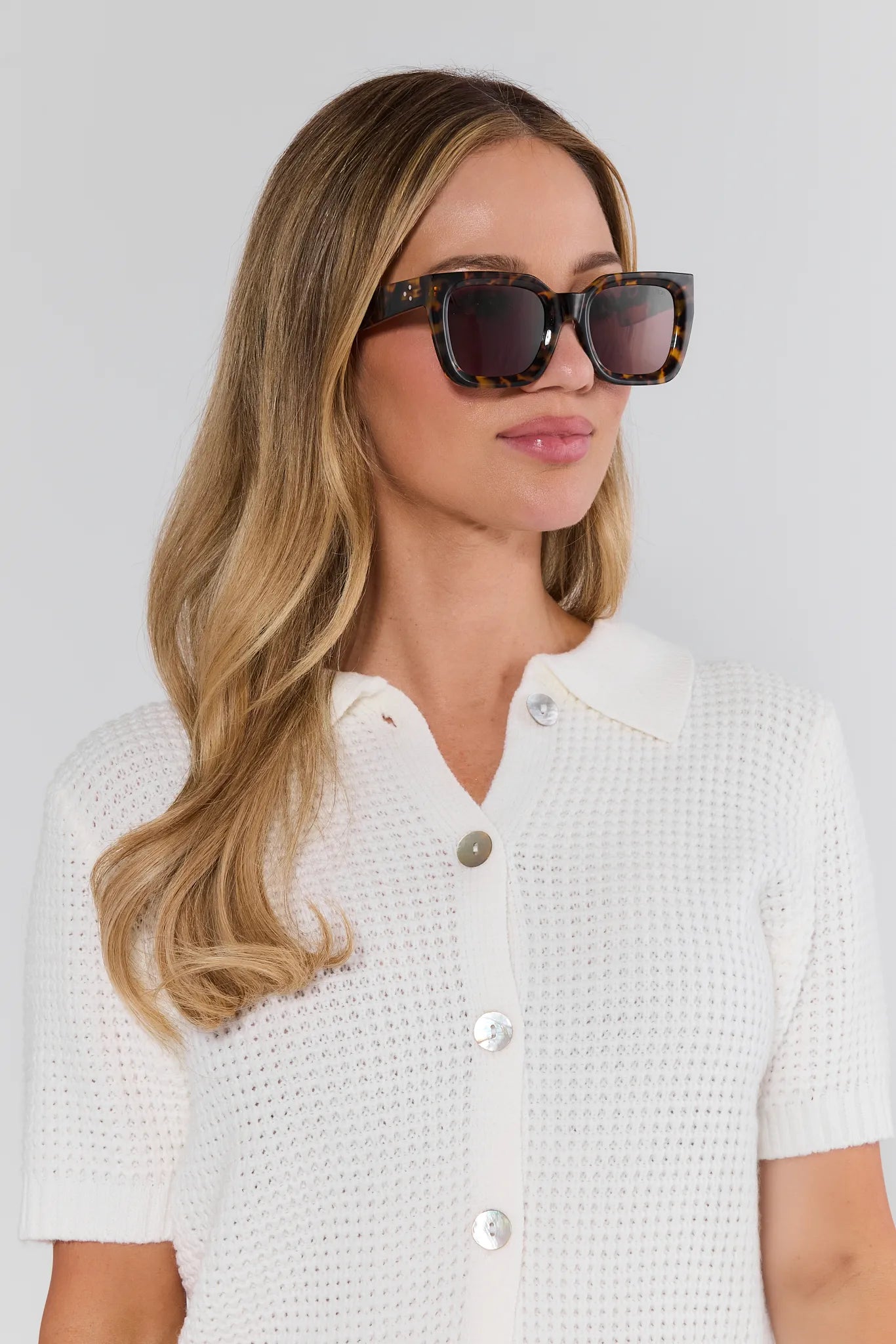 Woman wearing sunglasses and a white textured shirt against a light background